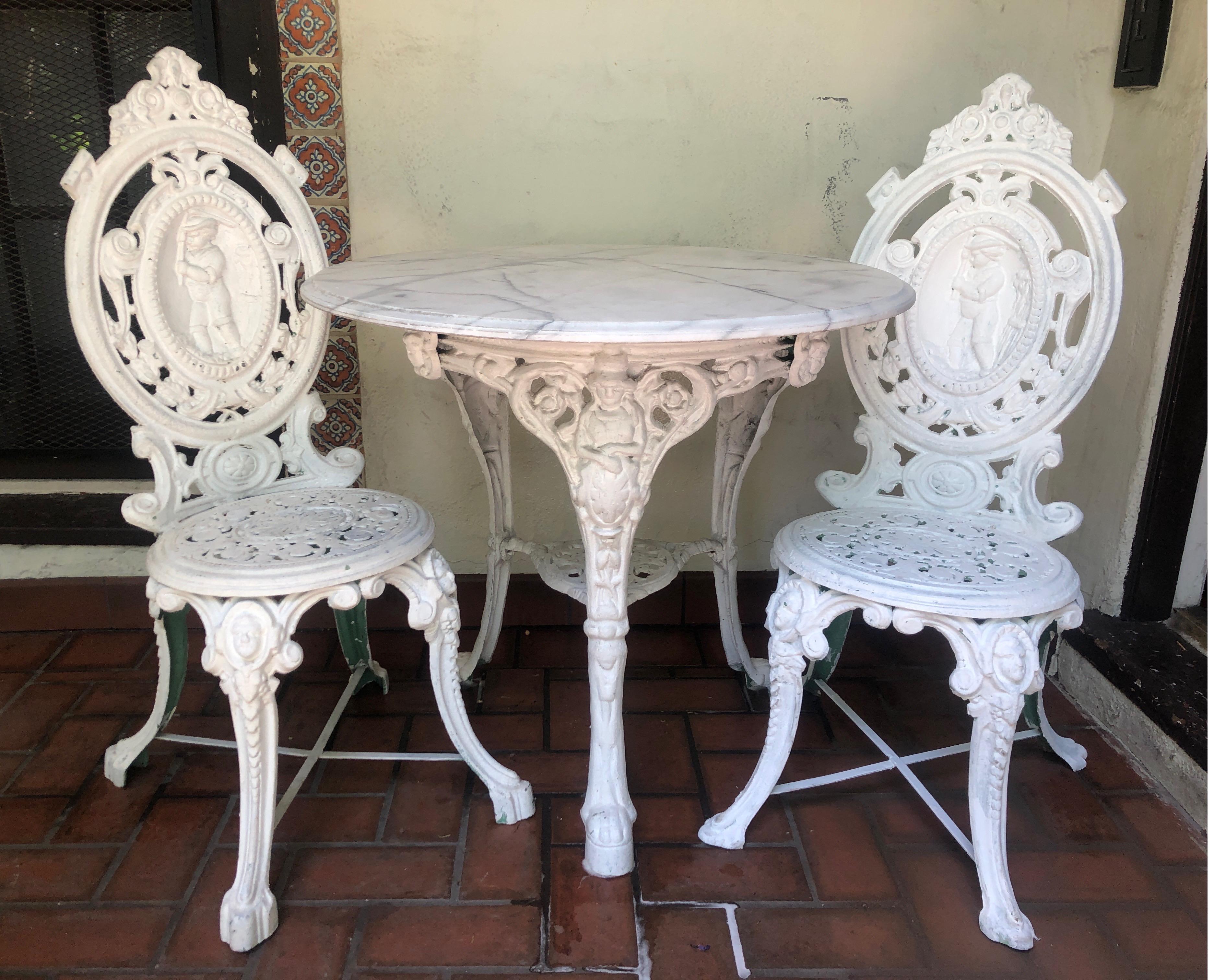 Direct from England.
Gorgeous white Victorian bistro/pub table set. Includes table and two chairs. 
Features a Carrera marble top with black/gray veining. 

Three upper legs have a figural 