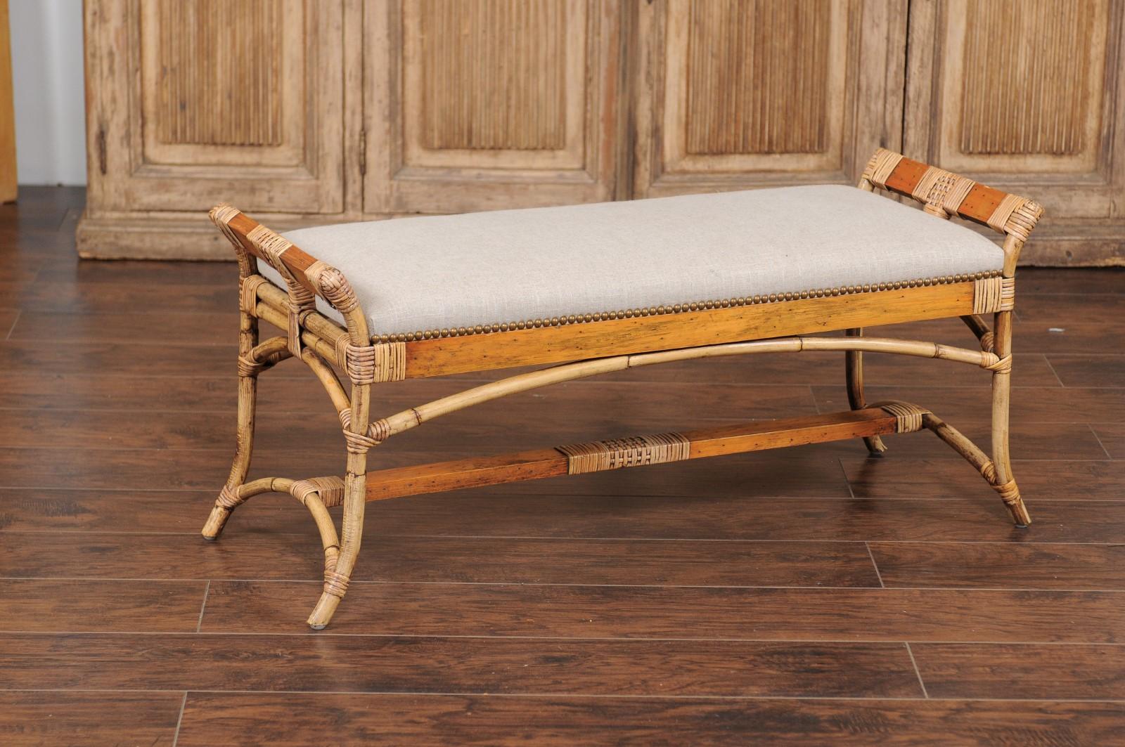 A vintage English bamboo bench from the mid 20th century, with out-scrolling arms and new upholstery. Born in England during the midcentury period, this stylish backless bamboo bench features two short splaying arms, surrounding a long rectangular
