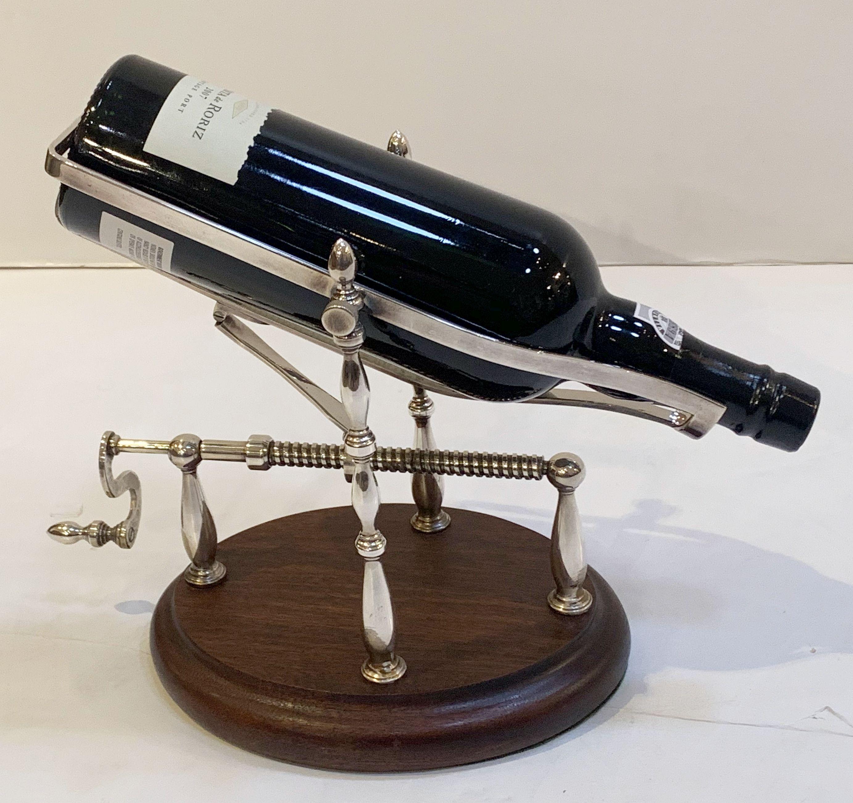 A handsome English port decanter or wine bottle pourer of silvered brass with turn screw action, on moulded ovoid wooden base.

A mechanical spirits pourer or decanting cradle is an artisan-like decanting device - turning the screw actuates the