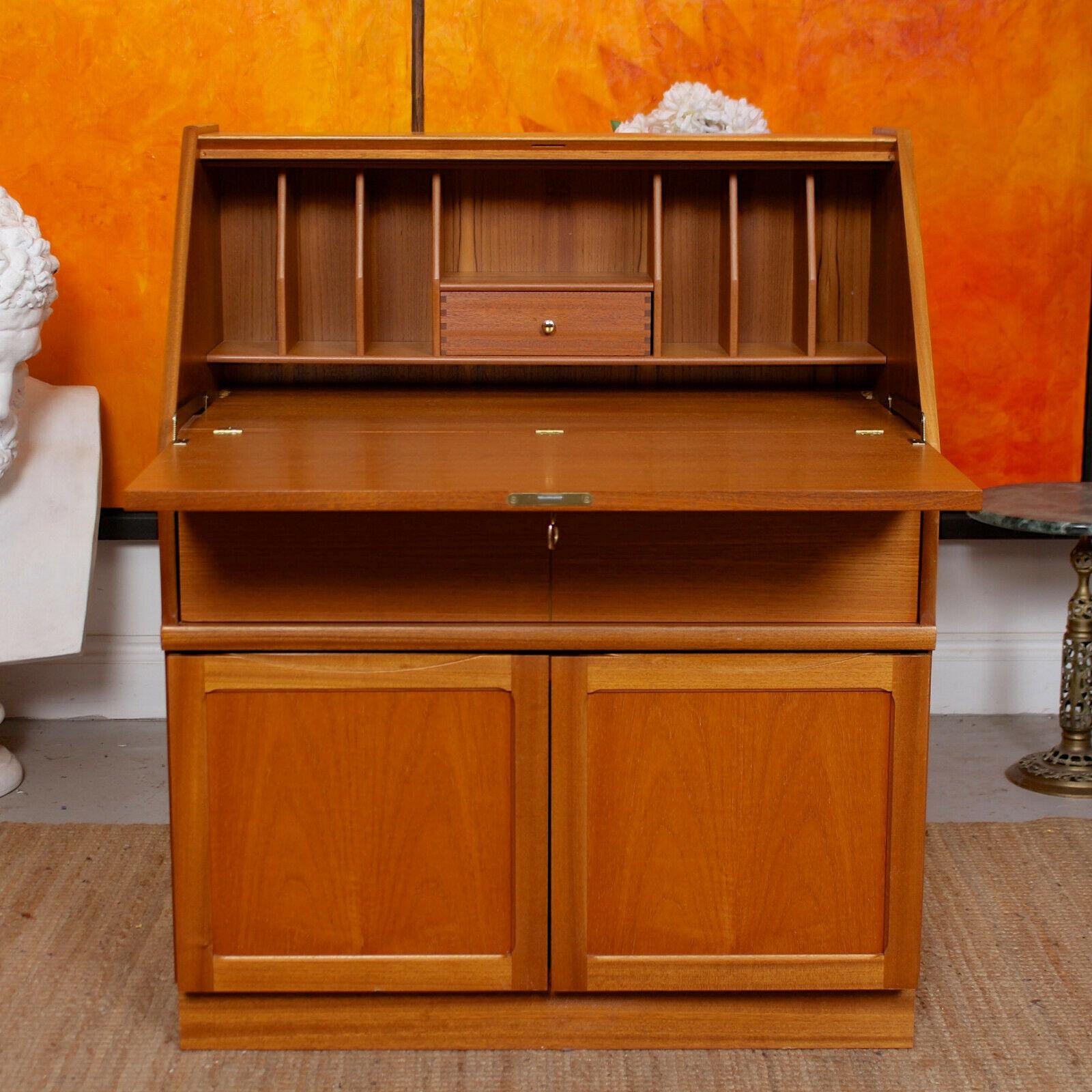 An impressive mid-20th century teak writing bureau.
The angled paneled fall flap enclosed a fitted interior comprising writing surface, miniature drawers, shelving and cubby holes. Fitted a long drawers below with carved inset handle and pair of