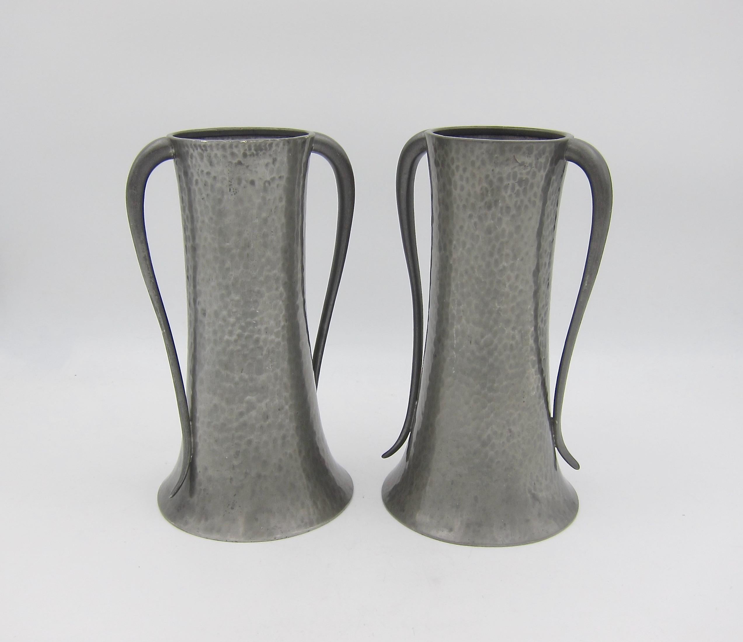A handsome pair of English hand-hammered vases from Walker & Co. of Sheffield in hand beaten pewter. The corseted bodies have planishing (hammer) marks overall and elegant, Art Nouveau curved double handles.

Good condition with some