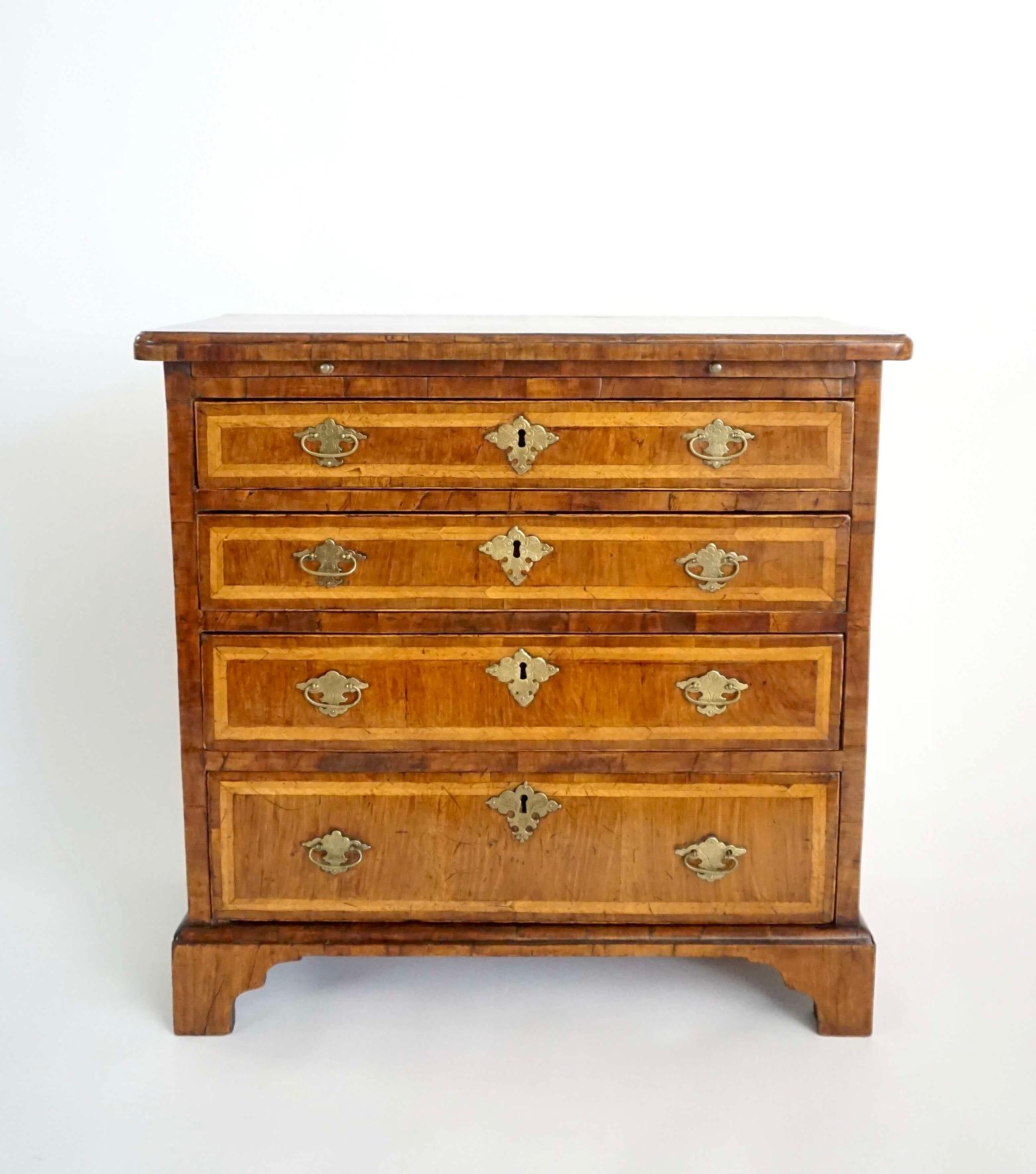 A fine and rare circa 1715 English late Queen Anne, early George I period small scale dressing or bachelor's chest, the walnut veneered case having bookmatched quarter-veneered and featherbanded top with a molded edge above a brushing slide and four