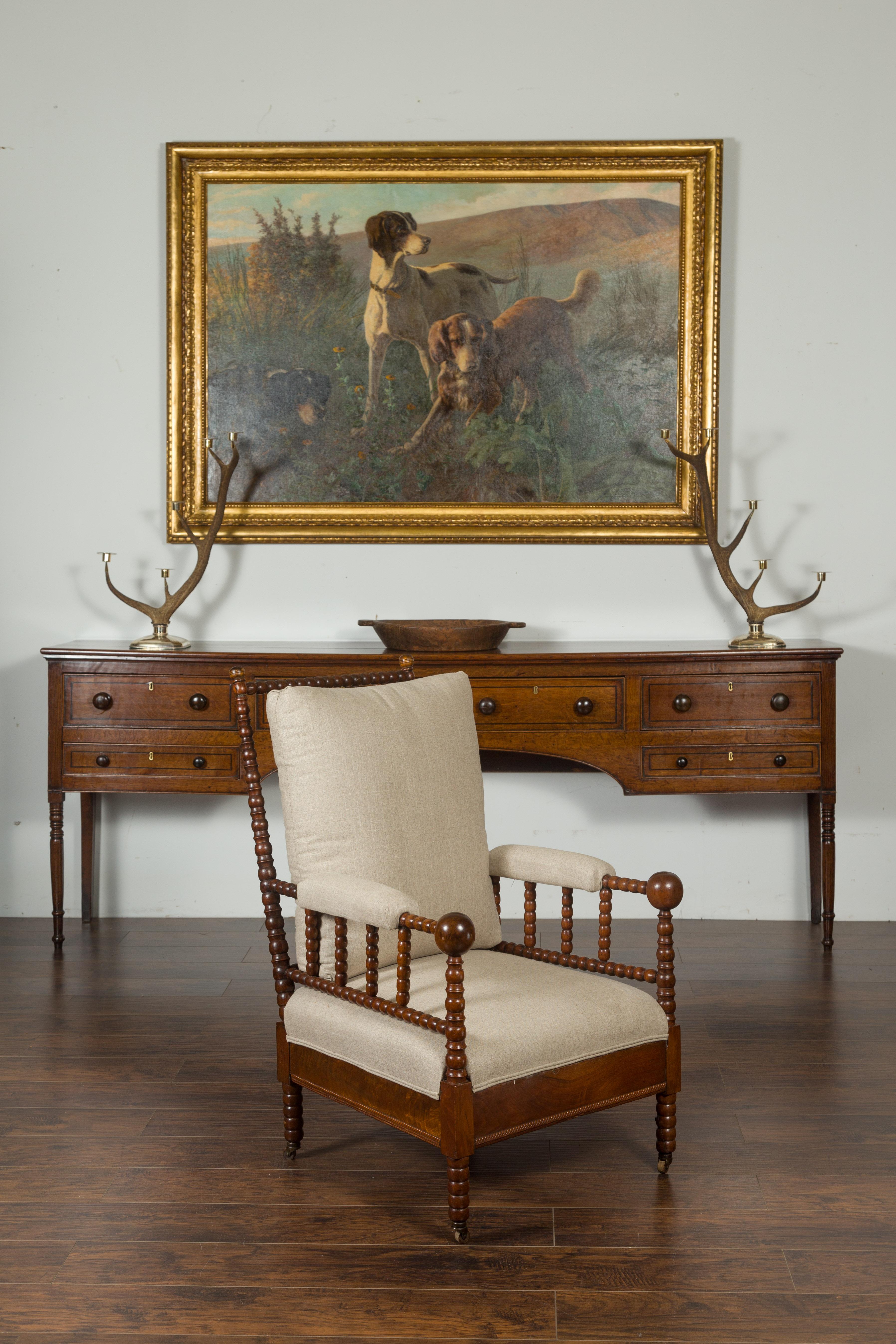 An English walnut bobbin armchair from the early 20th century, with new upholstery and casters. Created in England during the first quarter of the 20th century, this walnut armchair captures our attention with its bobbin structure and contrasting