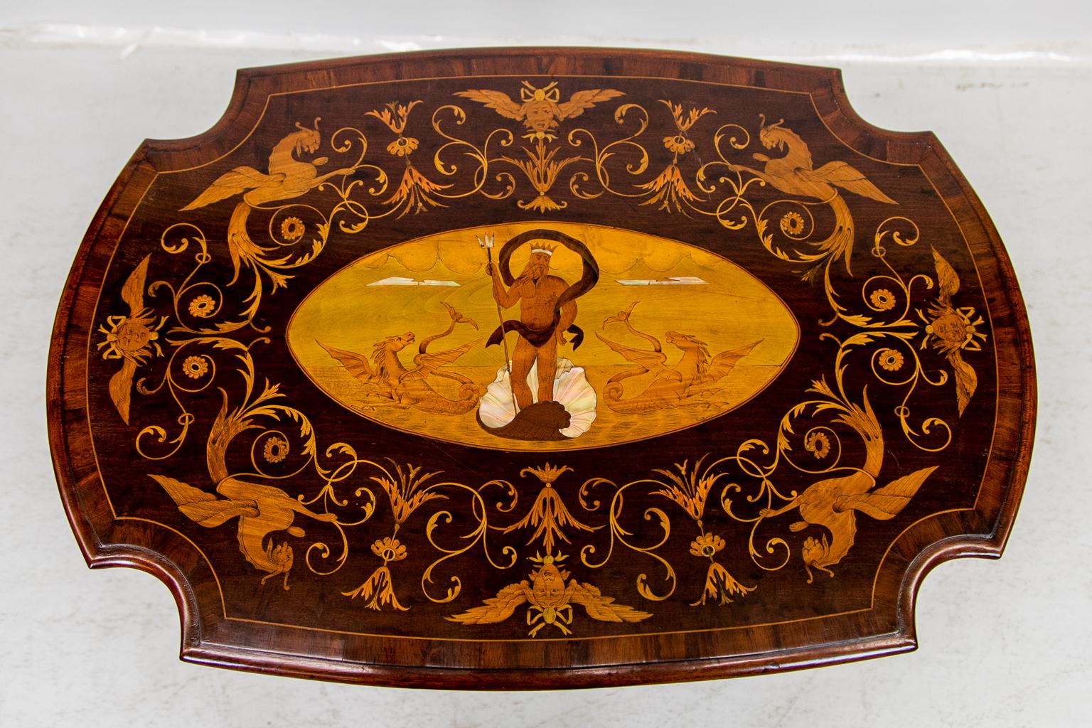 This center table is four sided and has a shaped molded top crossbanded with walnut and boxwood stringing. There is a central inlaid panel with an inlaid image of Poseiden standing in an incised mother-of-pearl shell. The inlaid images of clouds,