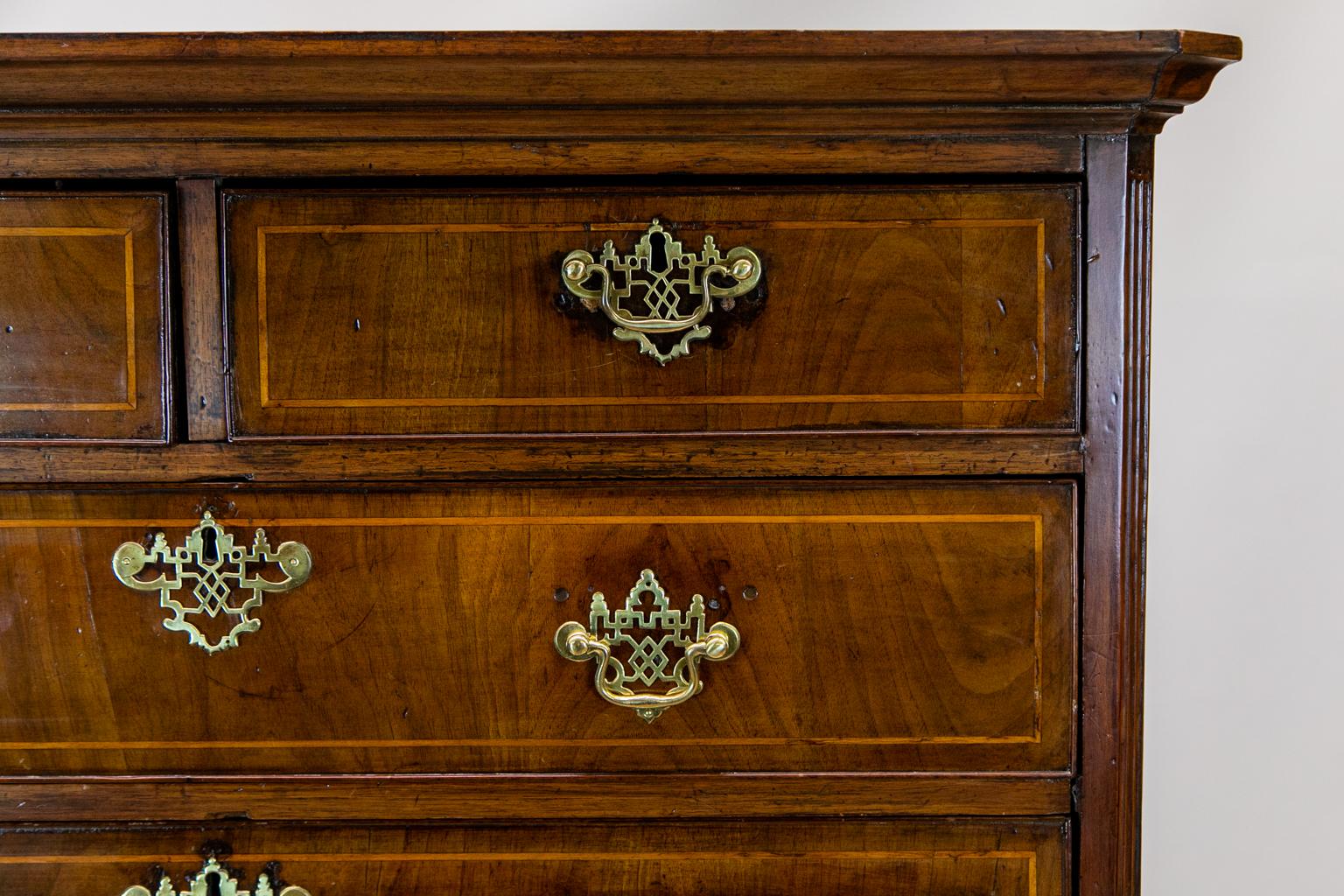 The drawers of this English walnut chest on chest are inlaid with boxwood string. The brasses are not original but are fine handmade replicas. There are ghost stains from previous hardware on the drawer fronts. The drawers are graduated from top to