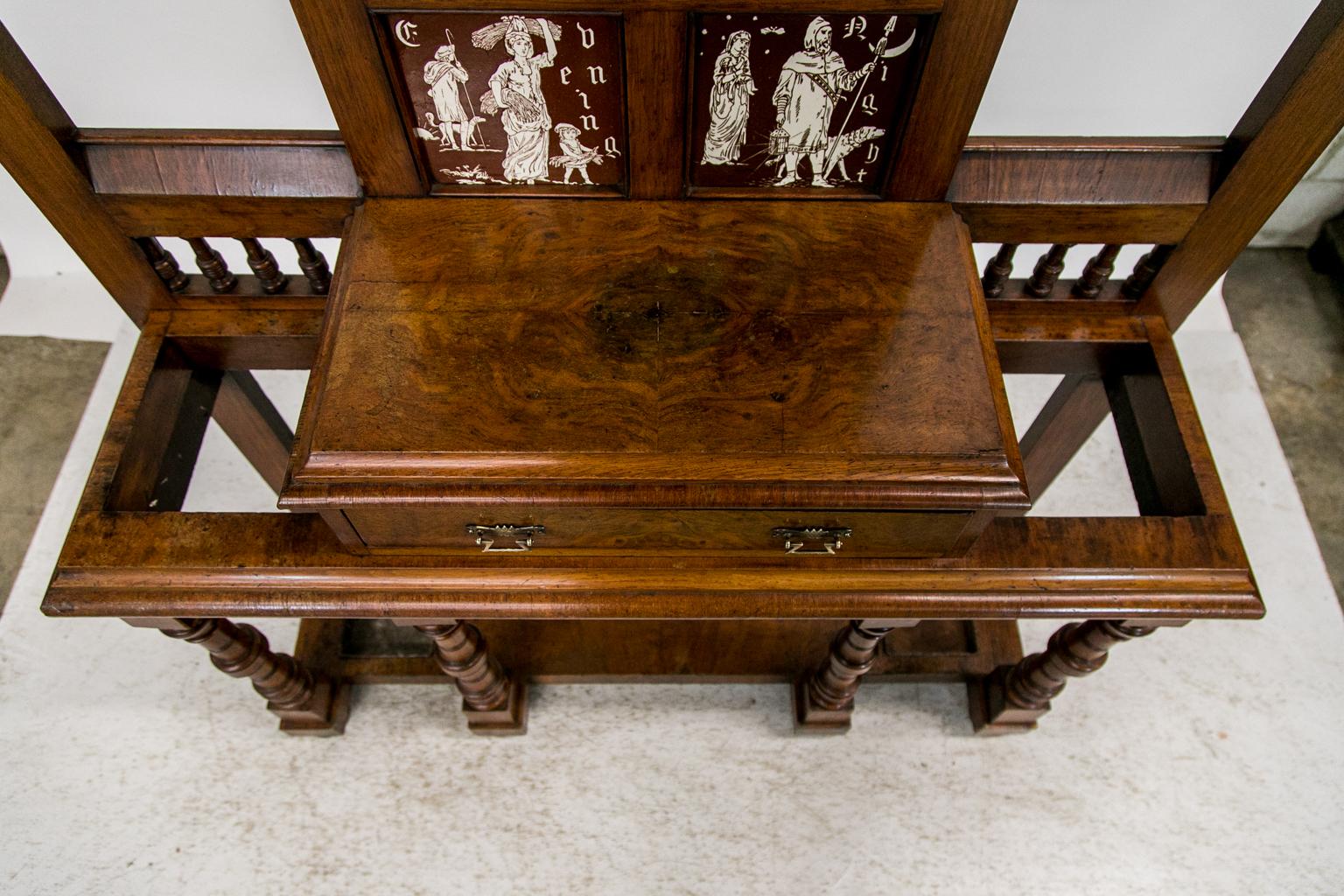 This walnut hall stand has an arched pediment with recessed graduated panels with a raised shield in the center. The frieze has a gallery of turned spindles above open panels on the sides that have beveled gothic arches supported by shaped brackets.