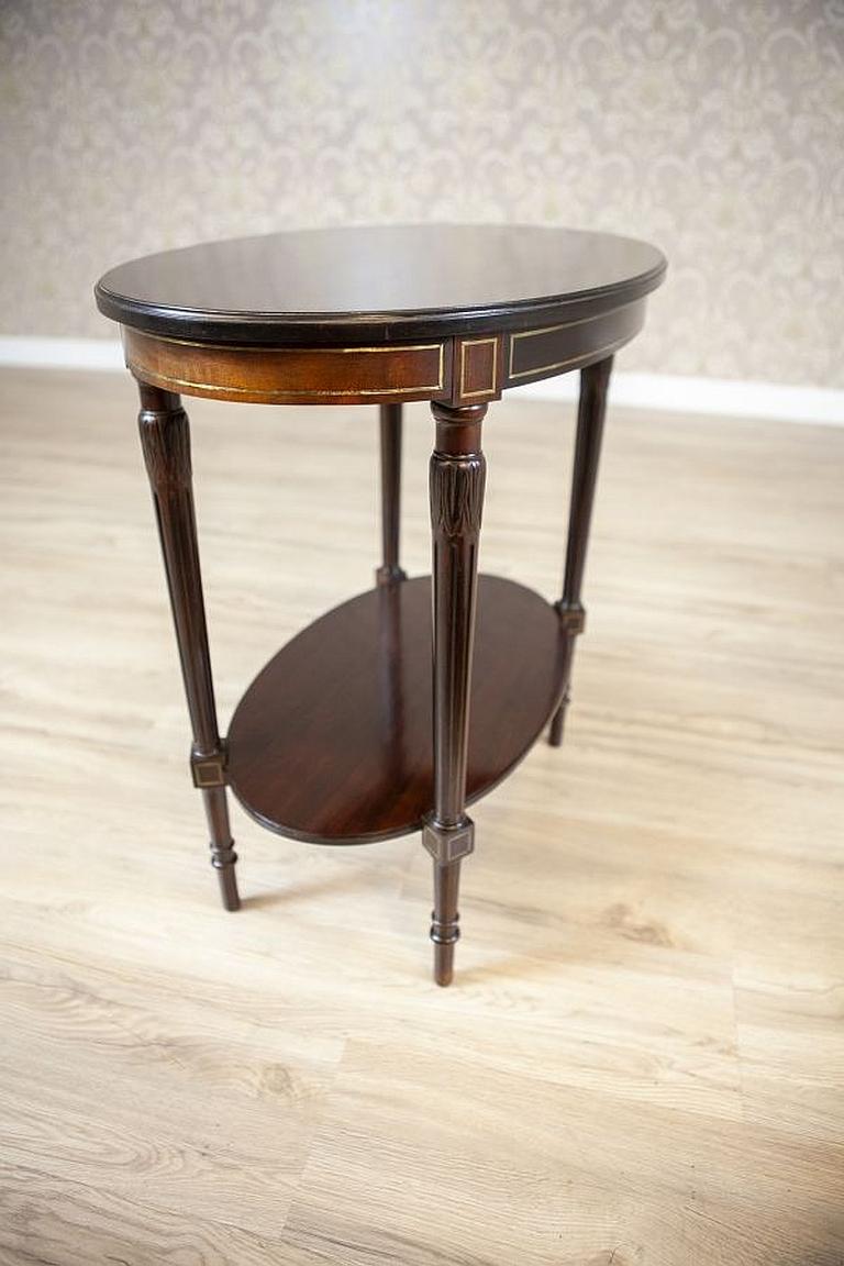 English walnut oval coffee table from the early 20th century

We present you this English walnut coffee table with a sliding top. The form of the piece is plain. There is a shelf at the bottom with inlays and a brass vein.
Presented table has