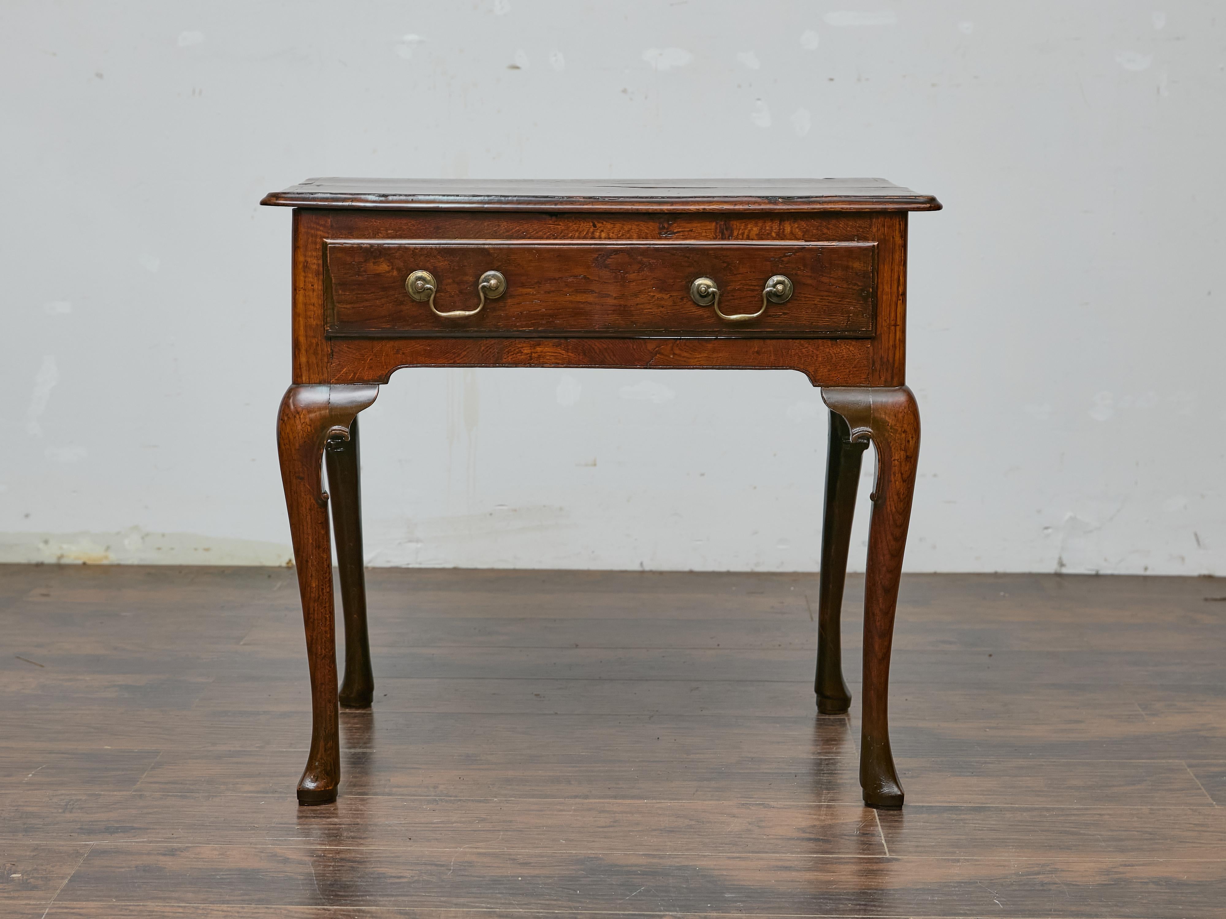 An English Georgian period walnut side table, circa 1800, with graceful proportions and timeless appeal. The single-drawer design offers both simplicity and function, featuring aged brass swan-neck pulls that contrast beautifully against the deep