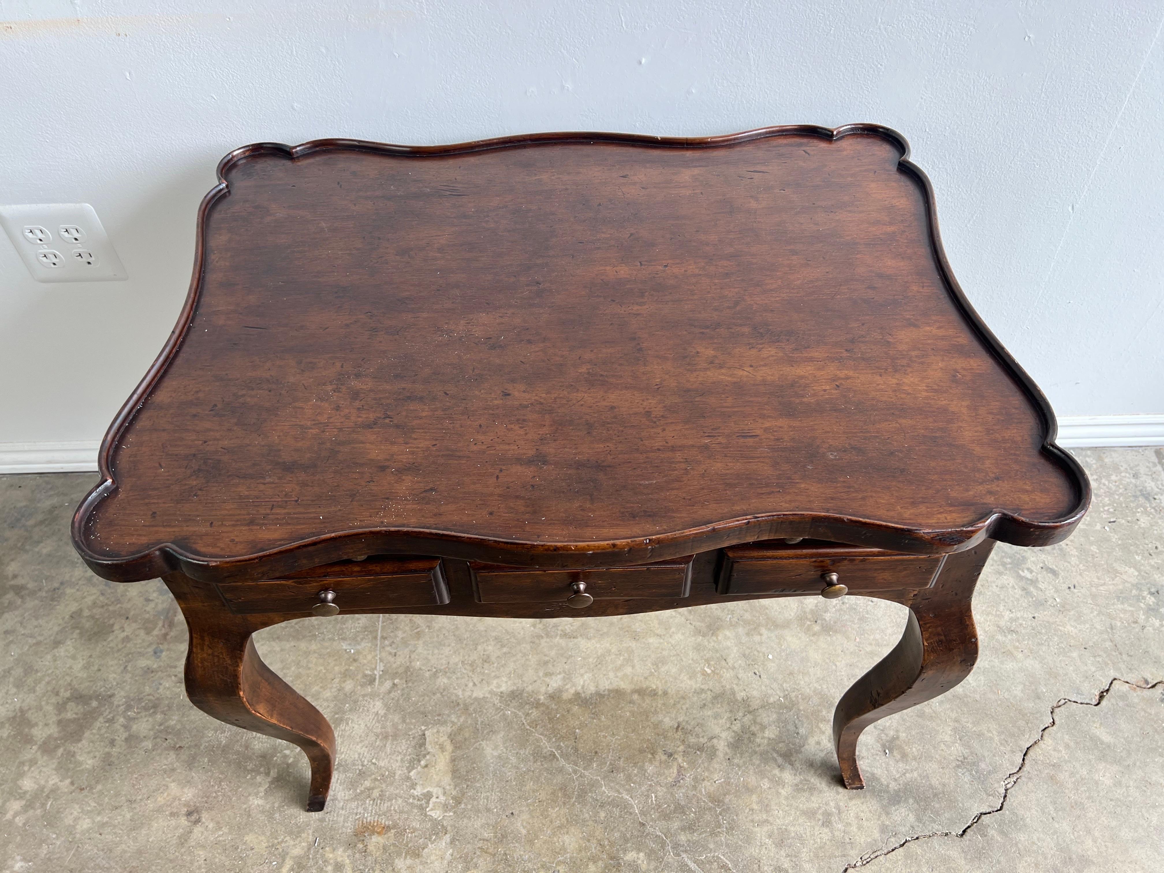 Early 20th century English walnut tea table with scalloped top. There are two drawers and a pullout shelf to use for writing.