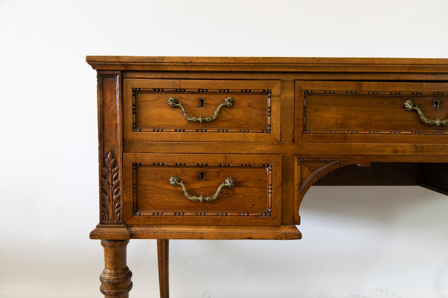 English walnut writing table has the original pulls, carved acanthus leaves on stiles, and fluted legs. The top has black leather with gold and blind tooling.
  