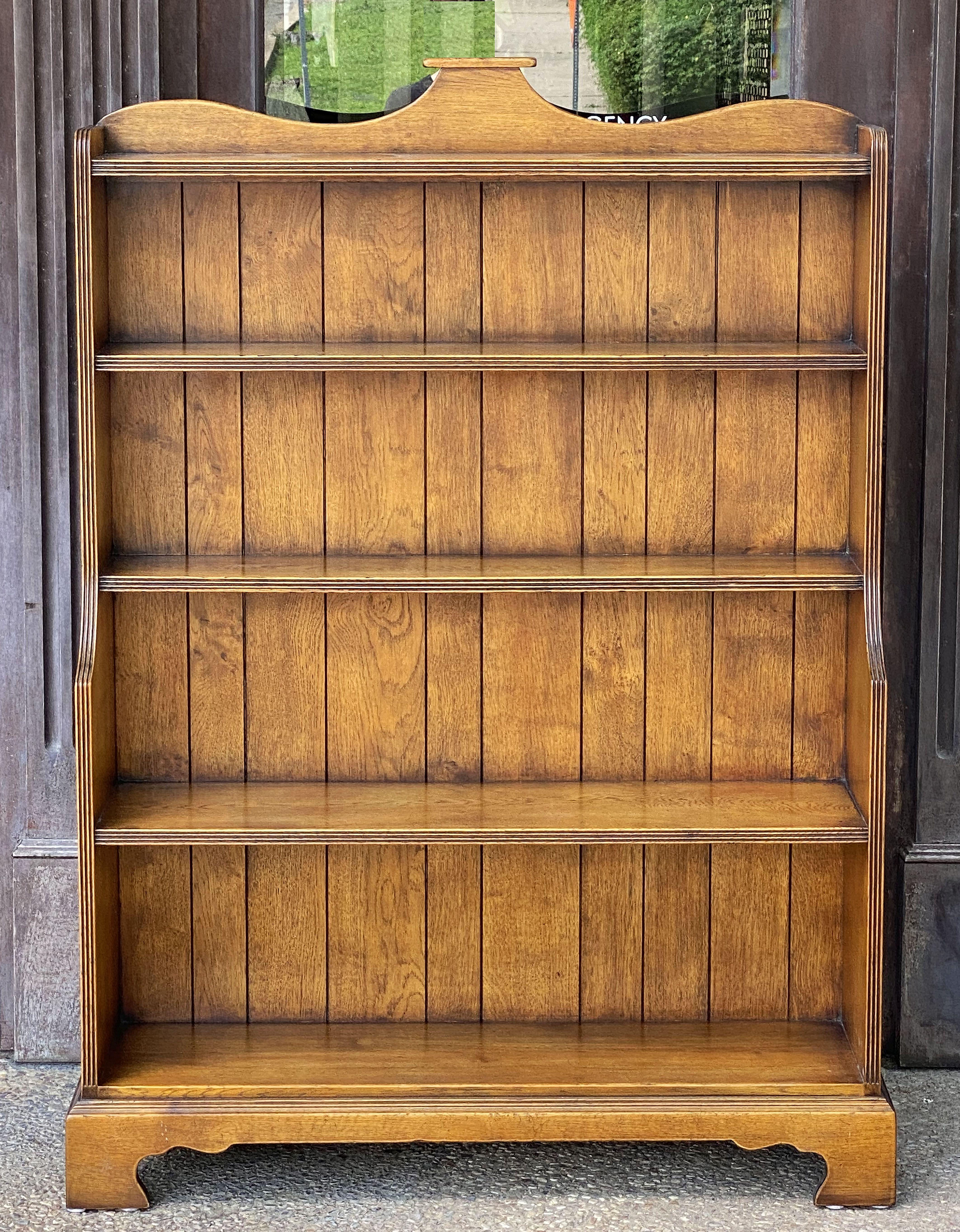 A fine English waterfall style open bookcase of oak, featuring a serpentine top gallery, with moulded panel sides, enclosing five open shelves of ascending size from top to bottom, and resting on bracket feet.