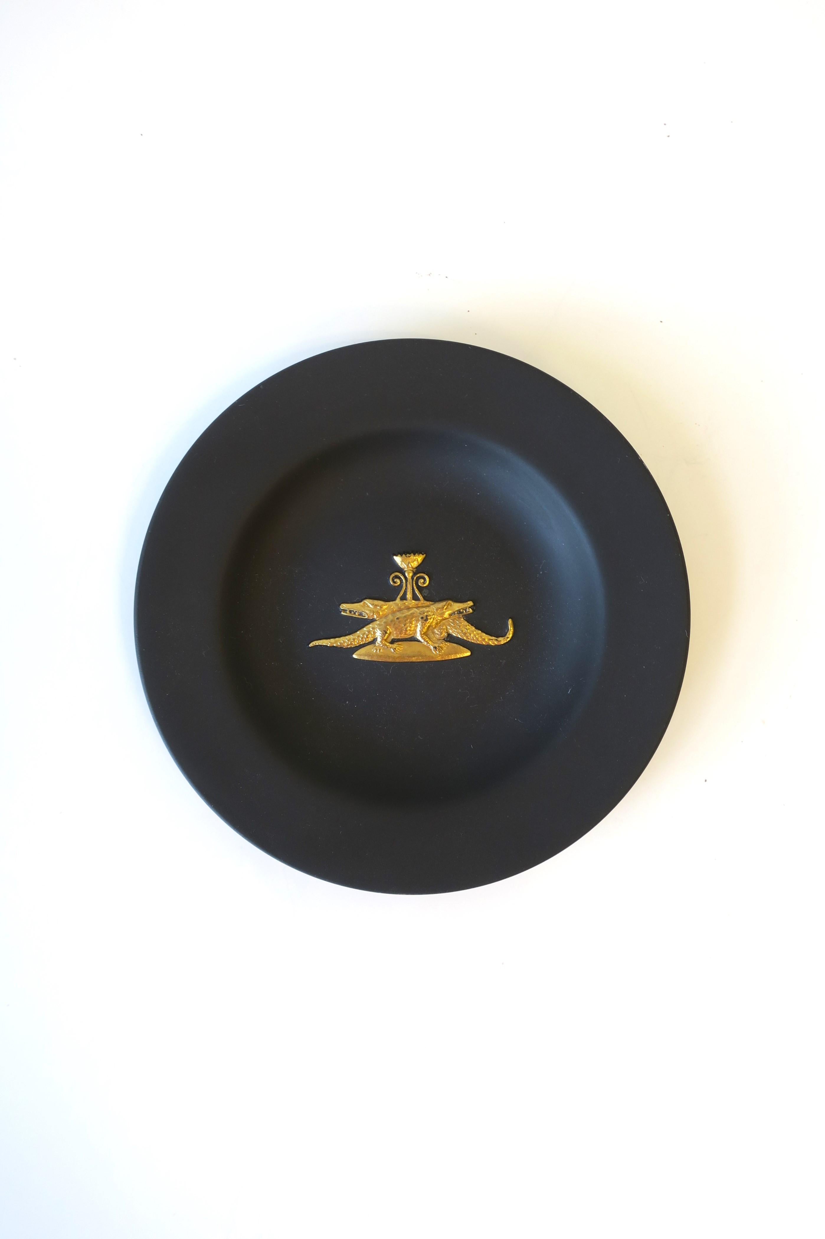 A rare English Jasperware matte black basalt and gold dish in the Neoclassical Revival style, by Wedgwood, England, circa late-20th century. A beautiful small piece with a gold raised relief of two alligators or crocodiles and an urn on a stand.