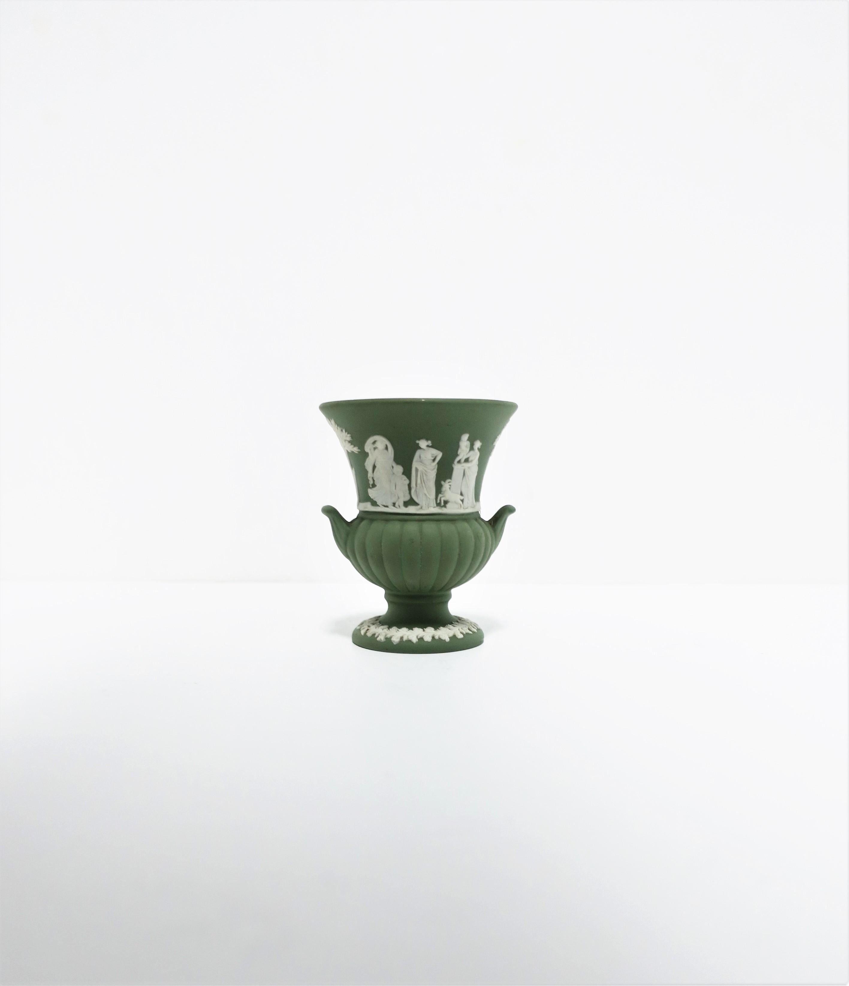 A beautiful, small, English Wedgwood Jasperware urn vase in the neoclassical design style, circa 20th century, England. Piece is a matte stoneware in a light green with a white neoclassical raised relief around center, a leaf design at bottom, and