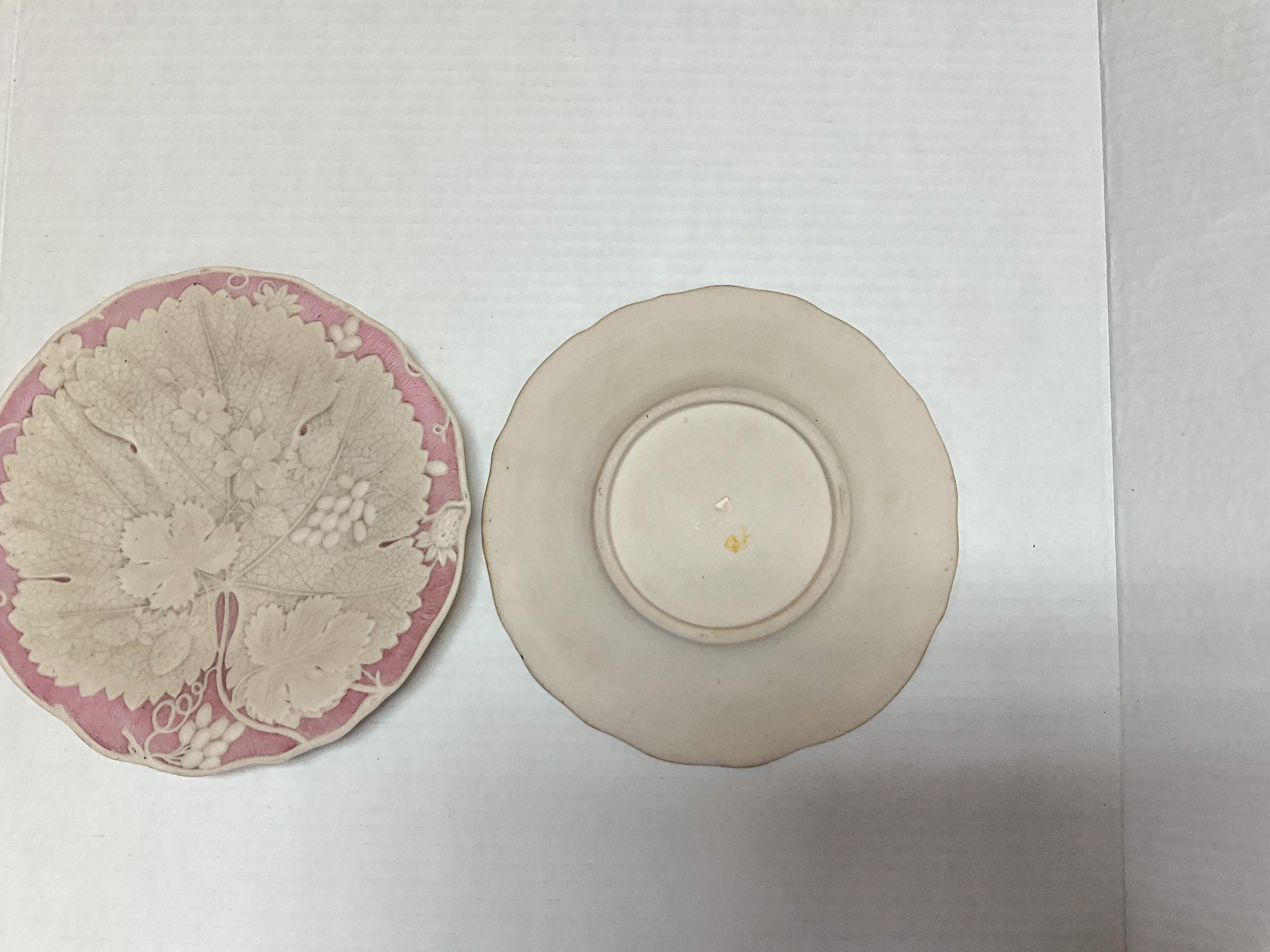 This is a lovely set of English pink and white basalt glaze decorative plates in the manner of Wedgwood. They appear to depict some sort of begonia leaf. The plates are unmarked and date to the later part of the 19th century.  One plate shows a bit