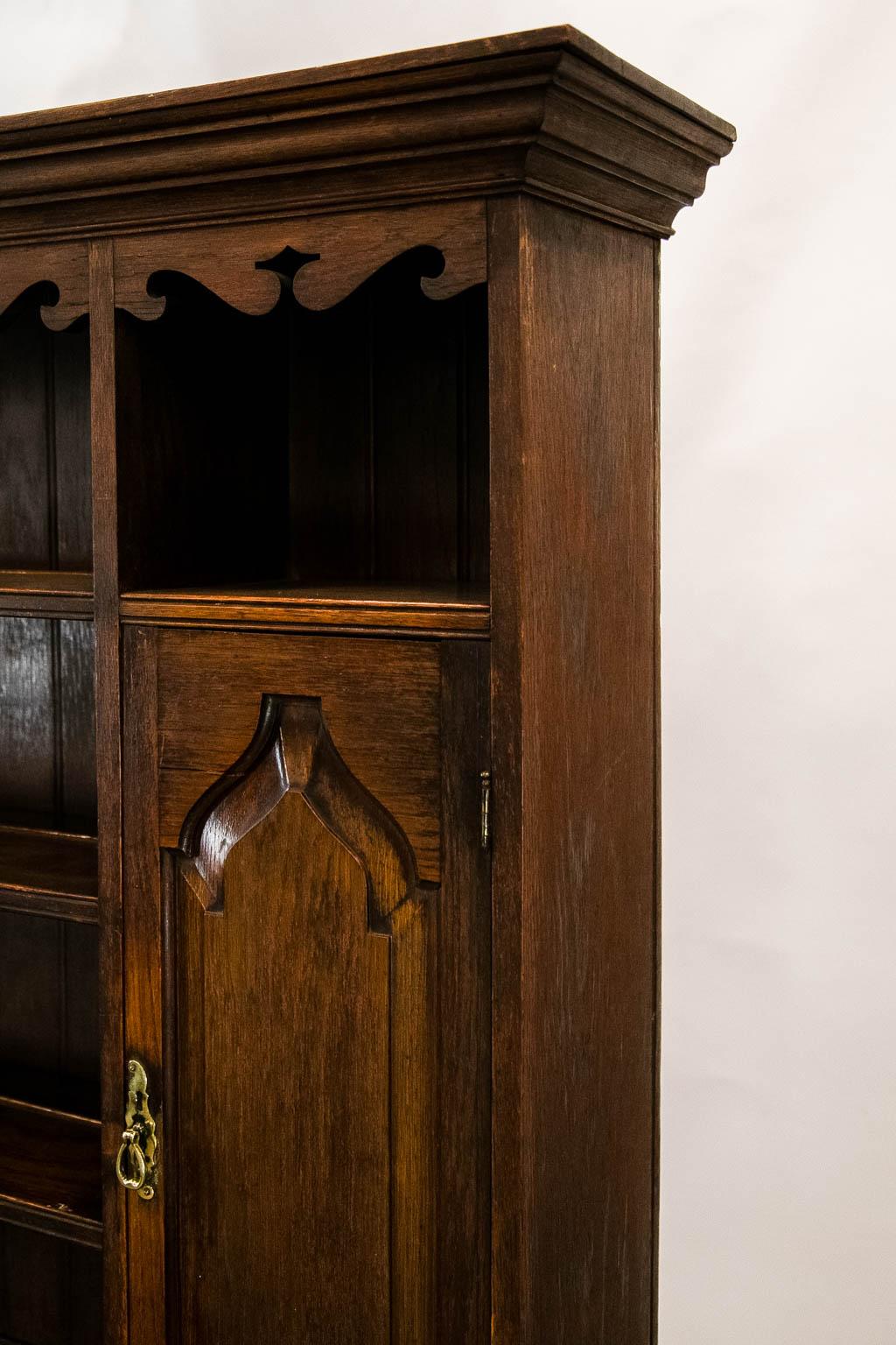 The cornice of this oak dresser has a scalloped frieze and two doors with raised gothic panels. The drawers have geometric moldings with a potboard below supported by bulbous legs.