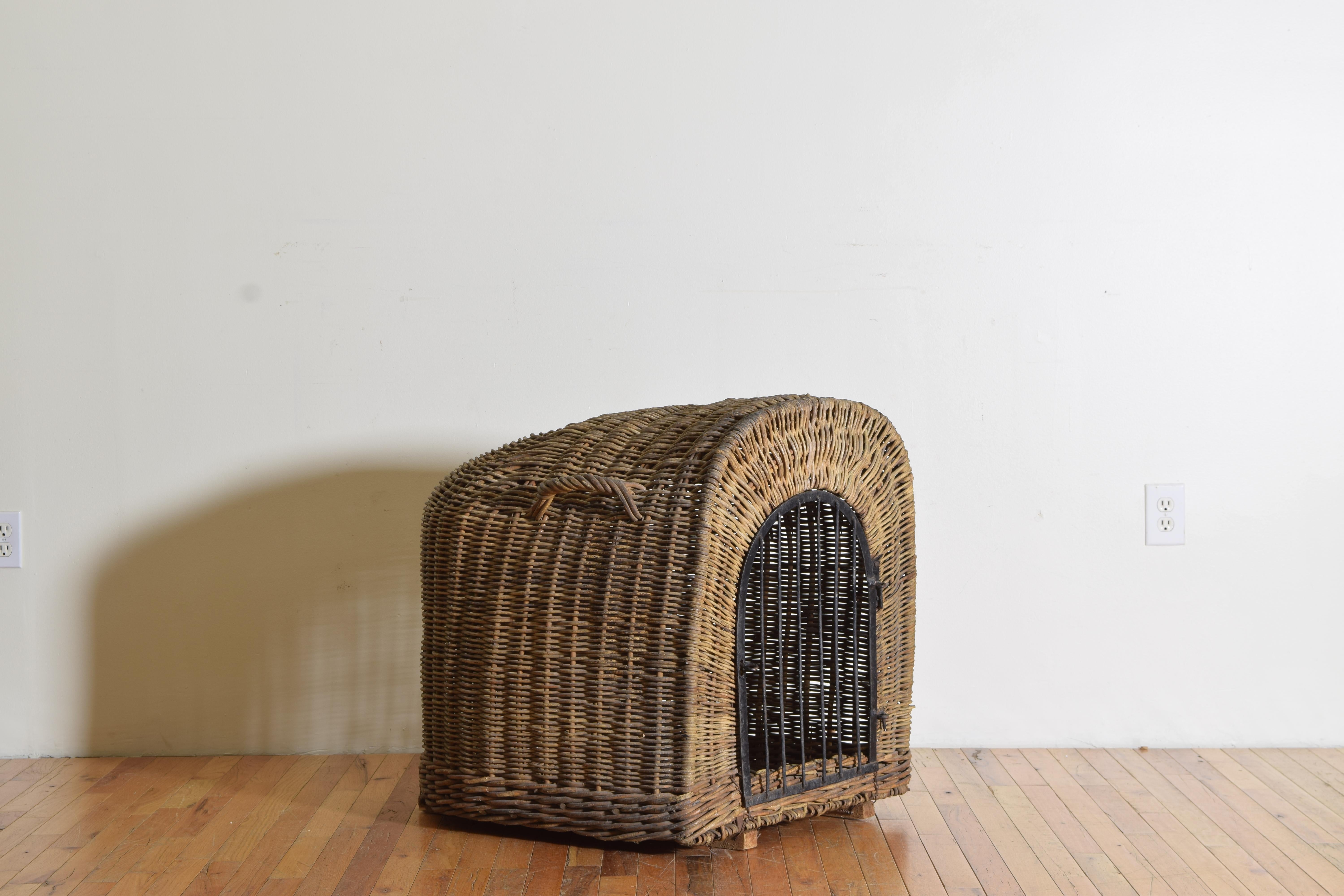 English wicker dog kennel with a removable hand-forged iron door. Having three handles for loading purposes, reinforced wooden lifts on the base to keep off the ground, and its original carved wooden and paper label tag. Structurally sound, in good