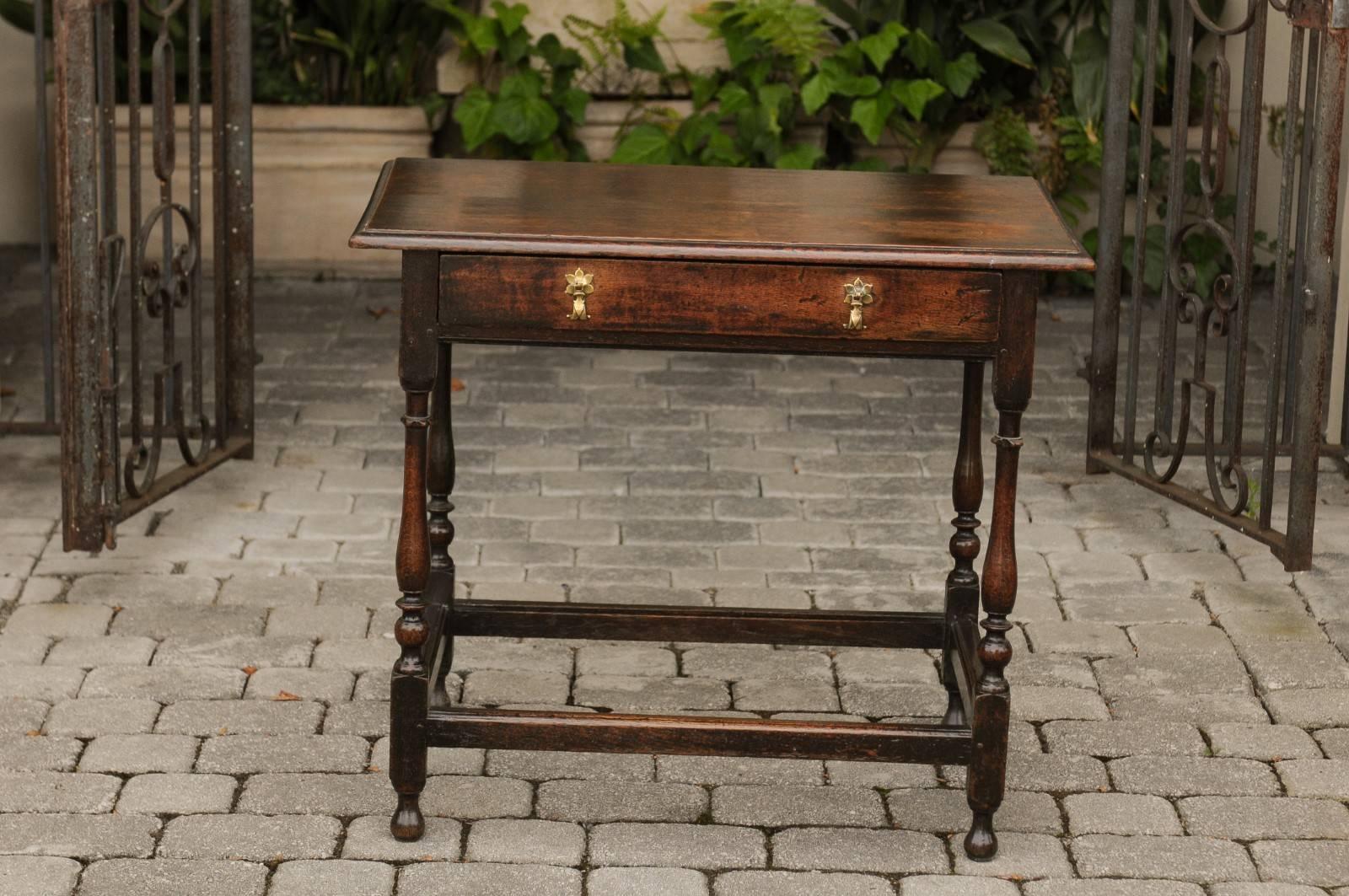 An English William and Mary style oak side table from the early 19th century with single drawer, turned legs and cross stretcher. This English oak side table features a rectangular top with bevelled edges, sitting above a long, single hand-cut