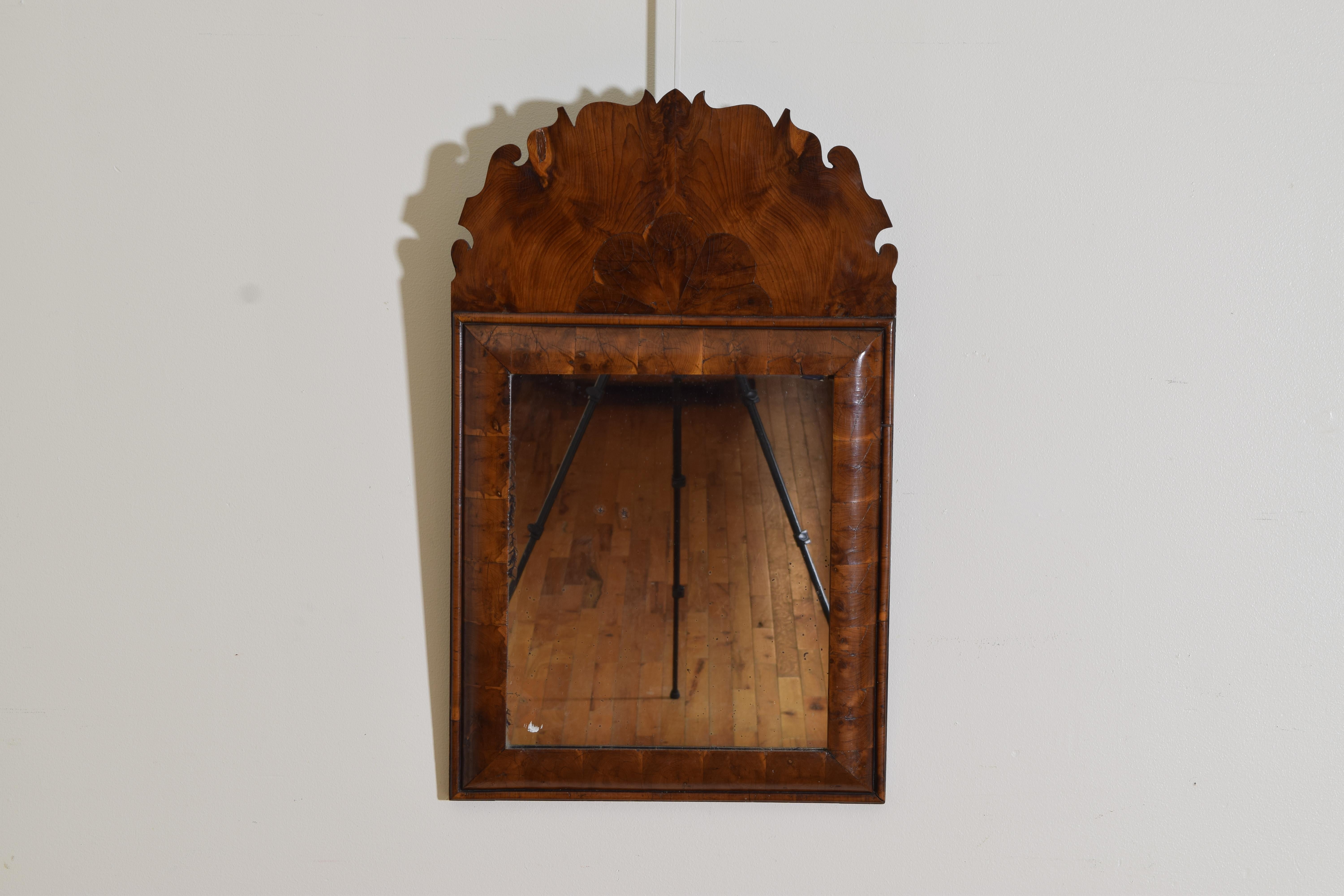Having a shaped crown covered in oyster walnut veneers above a cushion form frame covered in thick walnut veneers, retaining original mirrorplate 