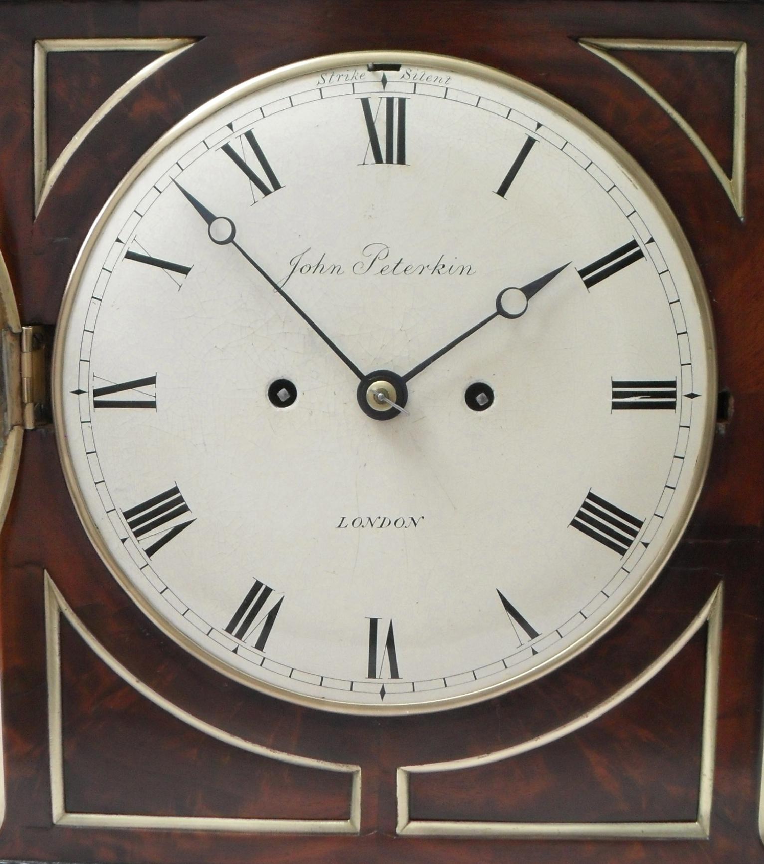 A very good quality English figured mahogany chamfer top bracket or table clock with ebony mouldings, brass string inlay, inset corner panels with brass moulded edges to the front stood on brass ball feet. The clock has fish scale sound frets and