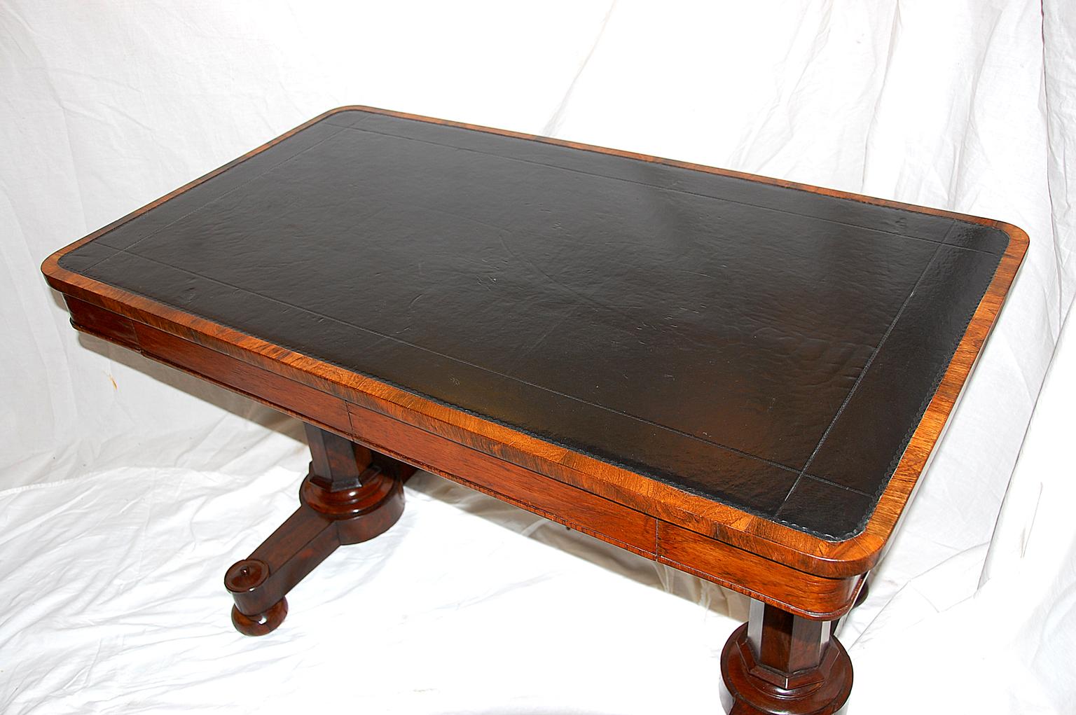 English William IV period rosewood pedestal writing table with old inlaid blind tooled leather writing surface in black, two drawers, faceted pedestal supports; circa 1835.