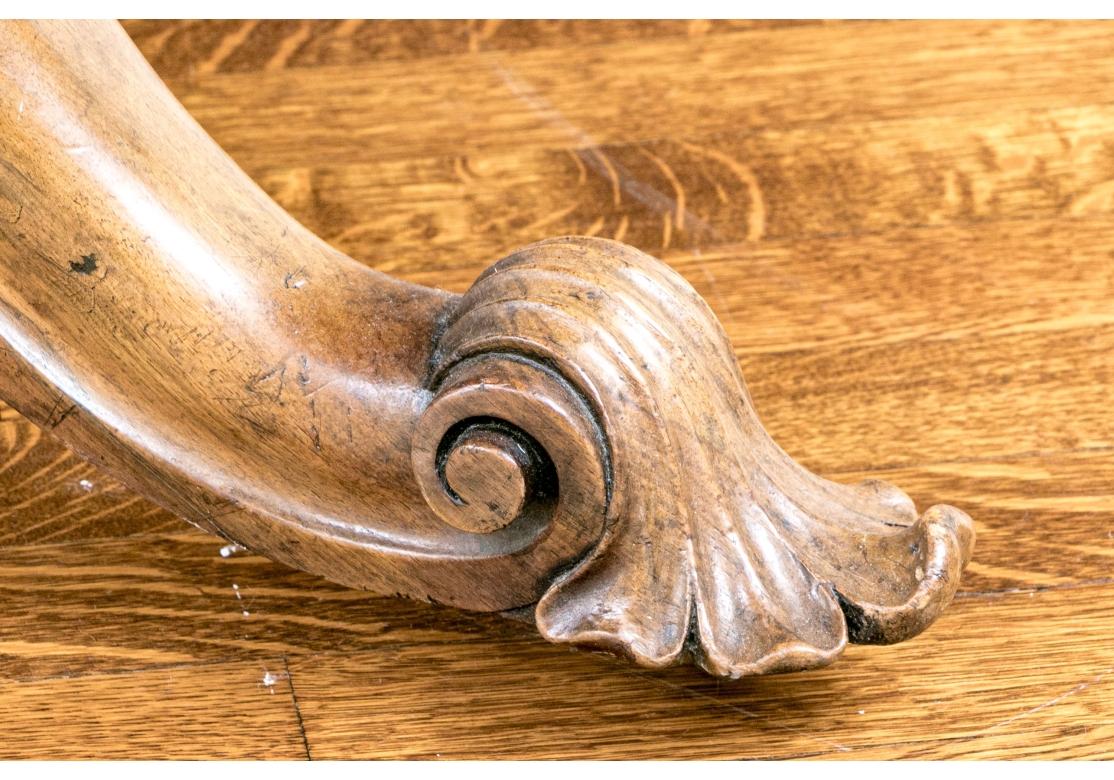 A fine English William IV style center table veneered in honeyed brown walnut with striking figuring at the center of a circular tilt top with a beveled edge. Raised on an elegantly carved column with ornately scrolled, foliate shoulders over a