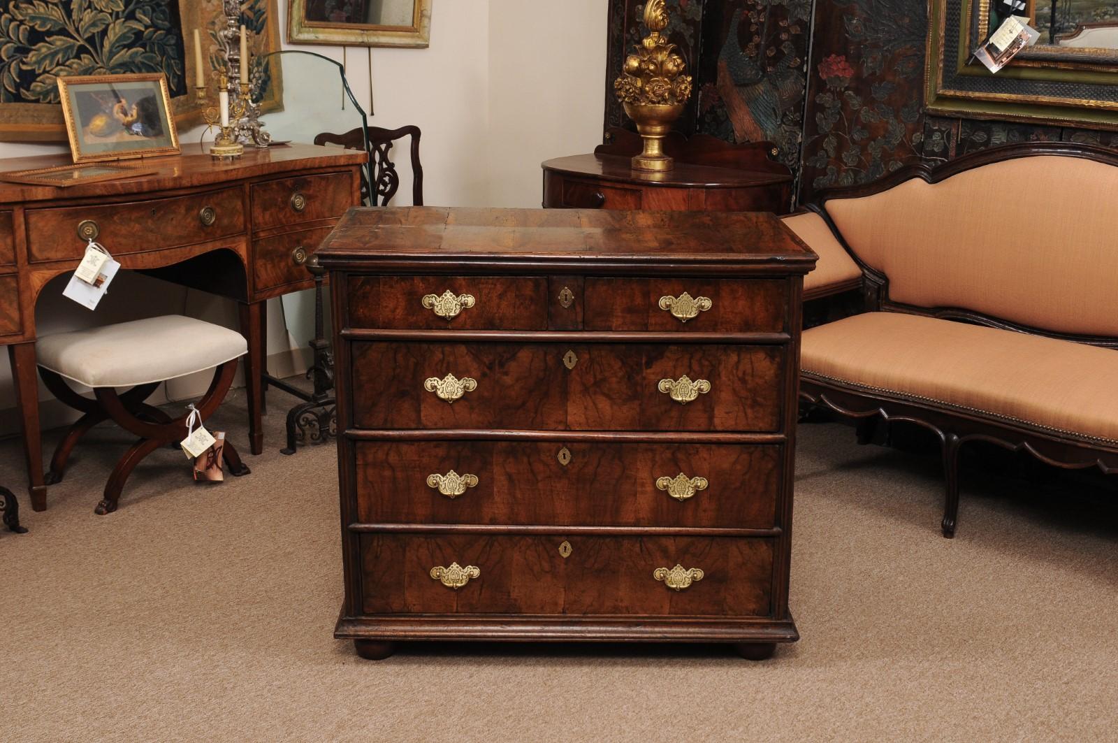 The English William & Mary chest in figured walnut with 2 short drawers above 3 long drawers terminating in bun feet. All the drawers with brass pulls and brass escutcheons.
