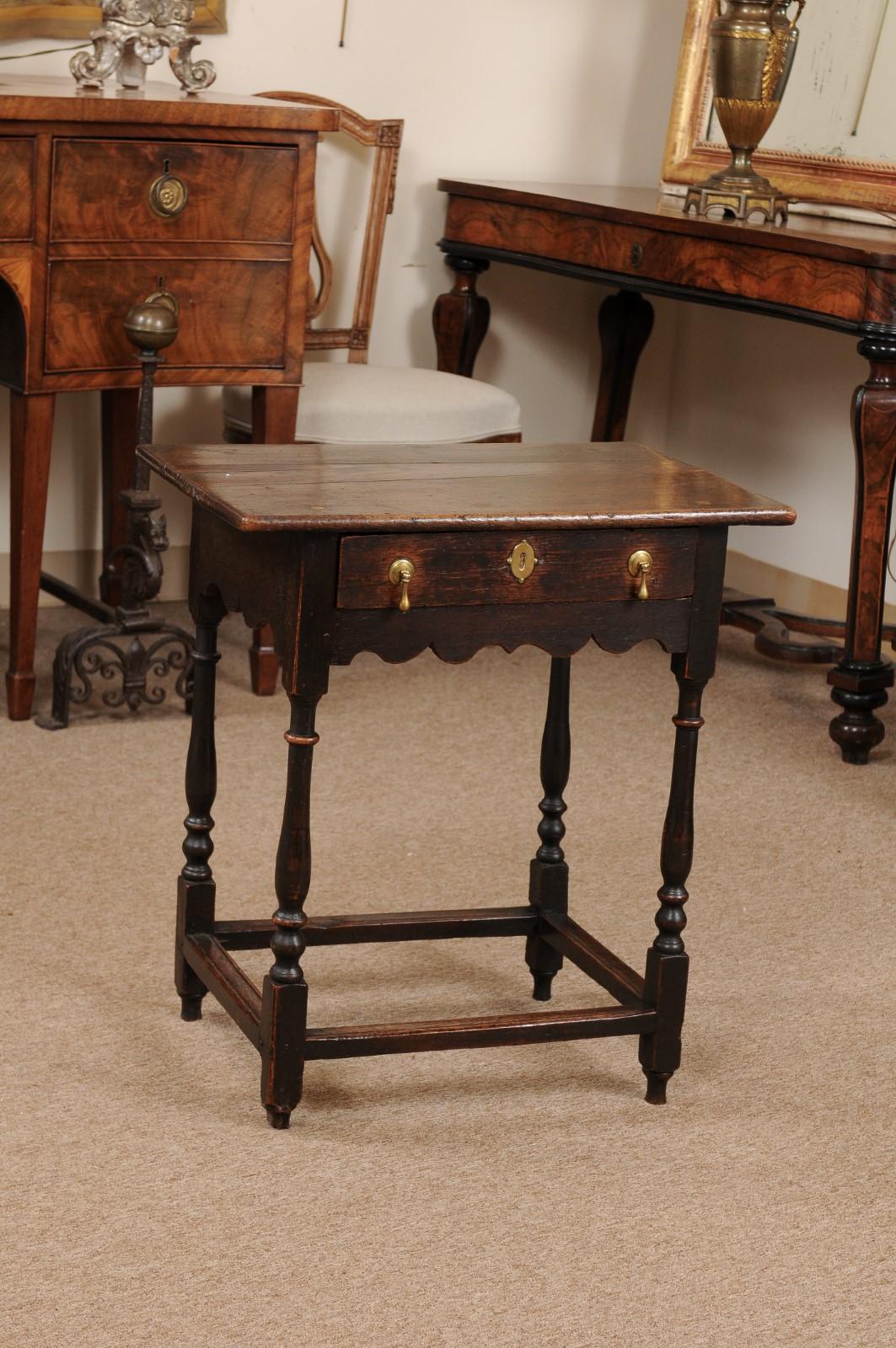 The English William & Mary style small oak side table with rectangular top, drawer with brass hardware and scalloped apron below. All resting on turned legs joined by box stretcher.