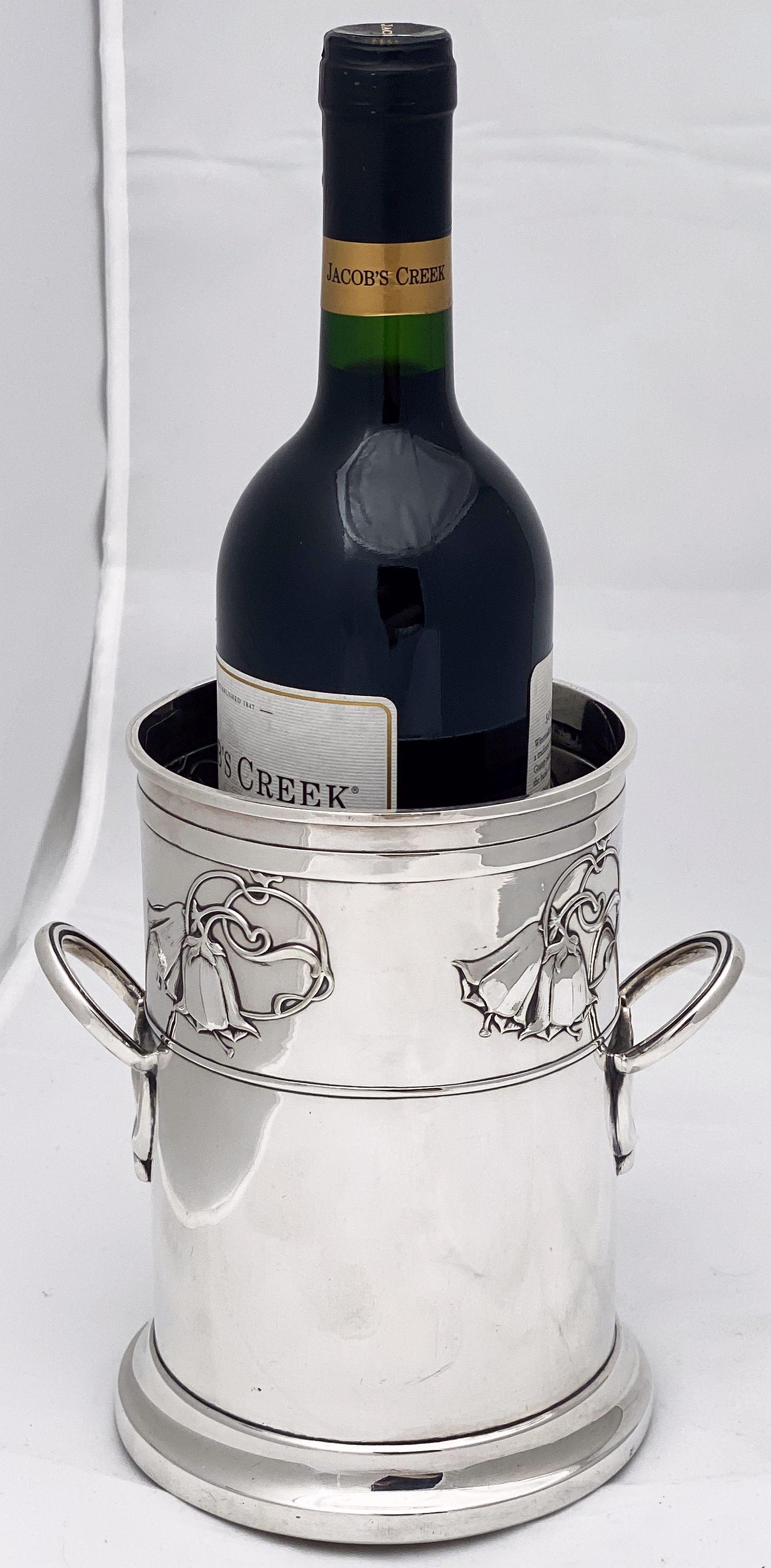 A handsome English wine and champagne bottle display holder or coaster of fine plate silver, featuring a rolled top edge, stylish opposing handles, an embossed Art Nouveau design of flowers, and raised cylindrical base with wood and felt underside.