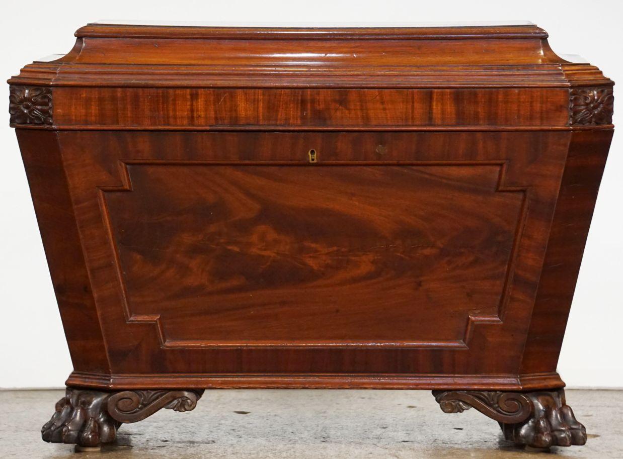 A fine English compendium for wine or cellarette wine cooler (sarcophagus) of mahogany, c.1840, featuring a center-paneled canopy (or mitered top) with cavetto moulded edge, opening to a felt-lined interior. The tapering body showing flame mahogany