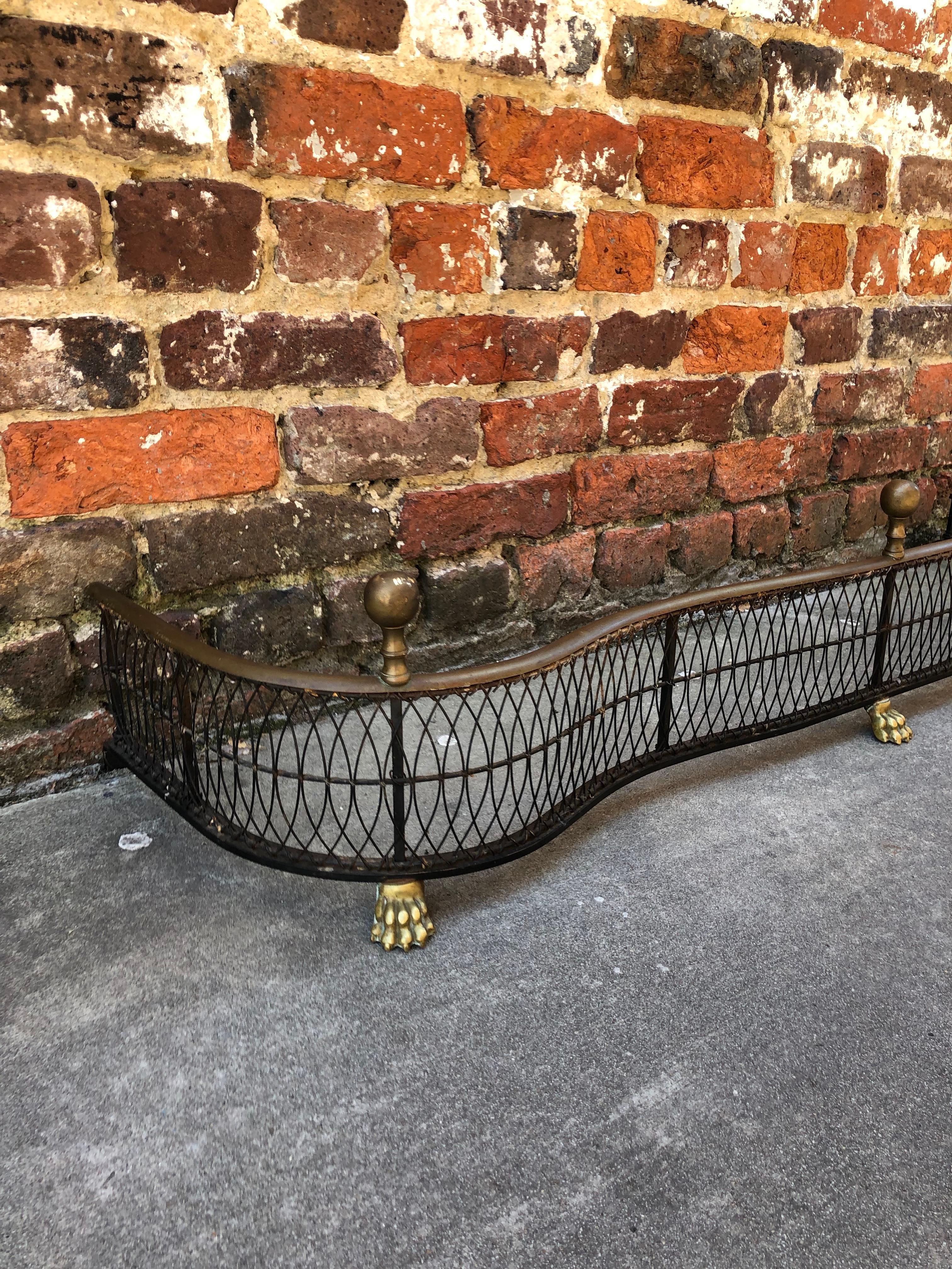 English wire and brass serpentine fender with finials and paw feet, circa 1850.