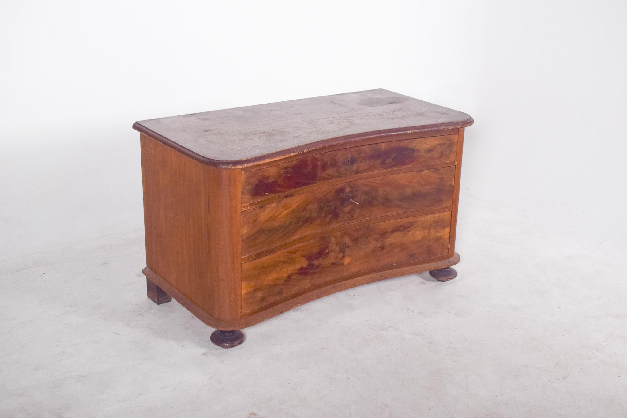 Serpentine chest of drawers with flat ball feet. Composed of three large drawers and a sturdy structure, the piece is reminiscent of the Biedermeier style or the transition to Art Deco, possibly dating from the early 20th century.
The drawer fronts