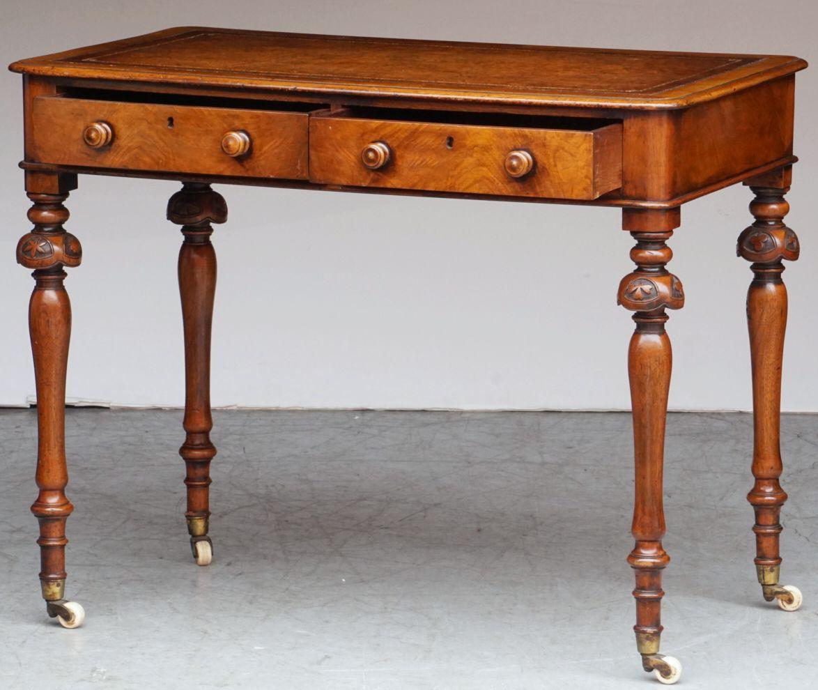 A handsome English writing table or desk of patinated mahogany from the 19th century, featuring a moulded wood and leather top embossed with gilt edge, over a frieze of two fitted drawers - each with two turned knob pulls and escutcheons, resting on