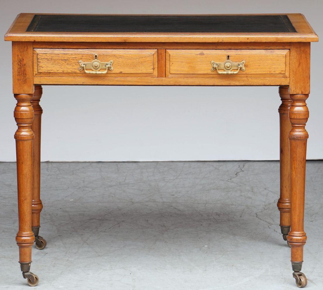 A fine English writing desk or table of patinated walnut from the 19th century, featuring an embossed black leather rectangular top, over a frieze of two fitted drawers - each with a brass handle in the Arts and Crafts style and two escutcheons, and