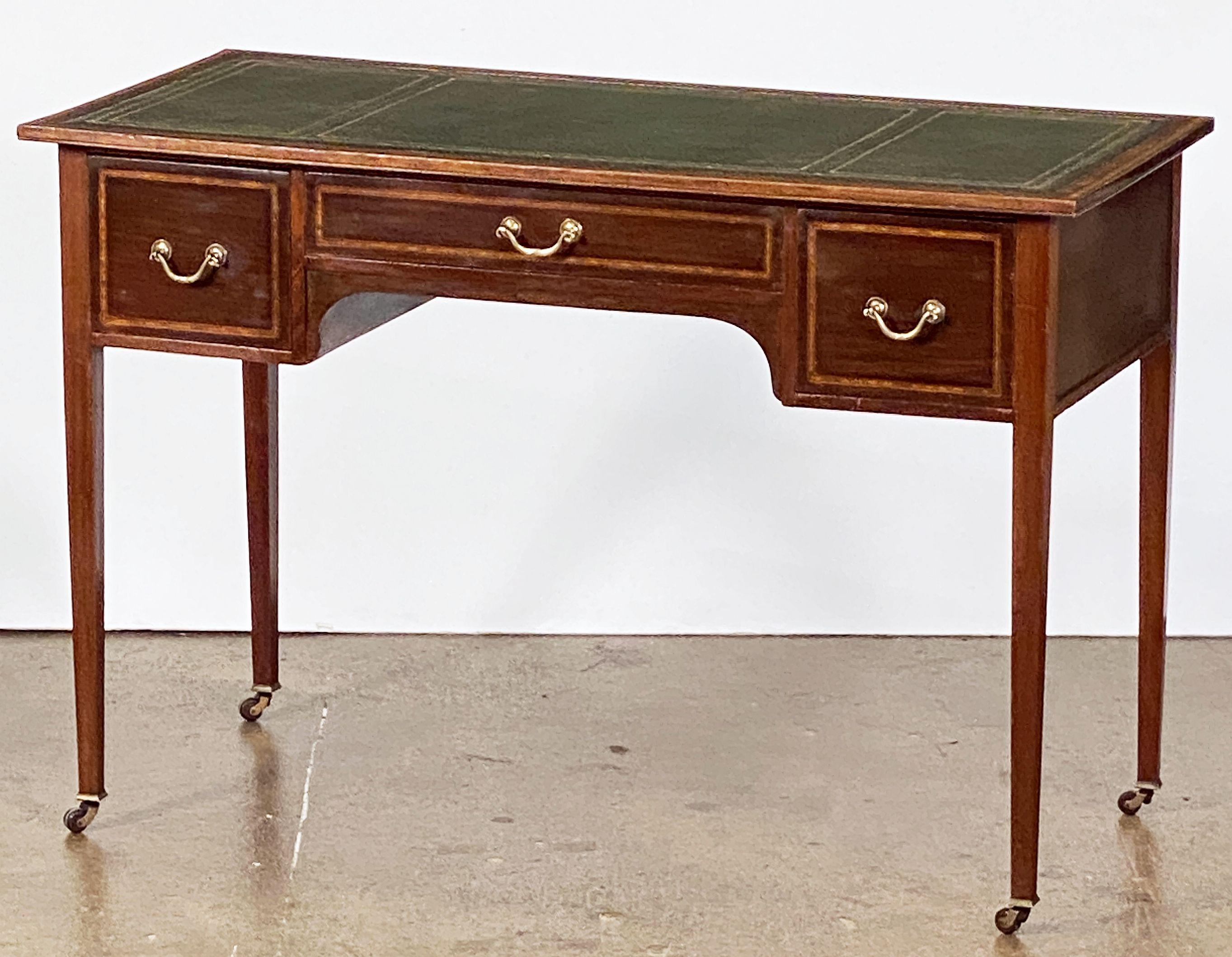 A fine English writing table or desk, featuring a moulded mahogany and gilt embossed green leather inset top with inlay around the facing edge, over a knee-hole frieze with three drawers, each with inlay and brass hardware, and set upon four tapered