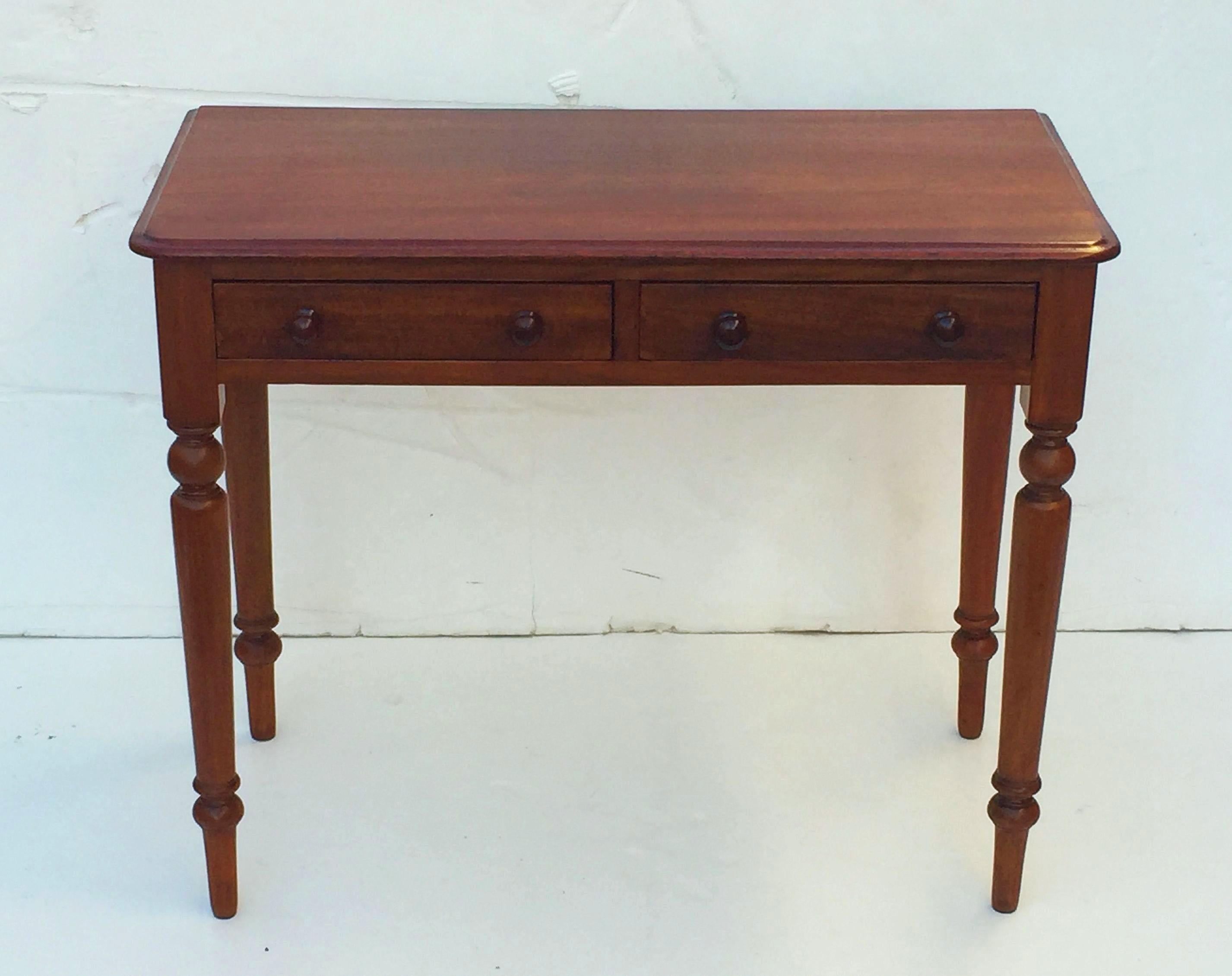 A fine English writing table or desk of mahogany featuring a rectangular moulded top over a frieze of two drawers, each drawer with two knob pulls,  and resting on turned legs.