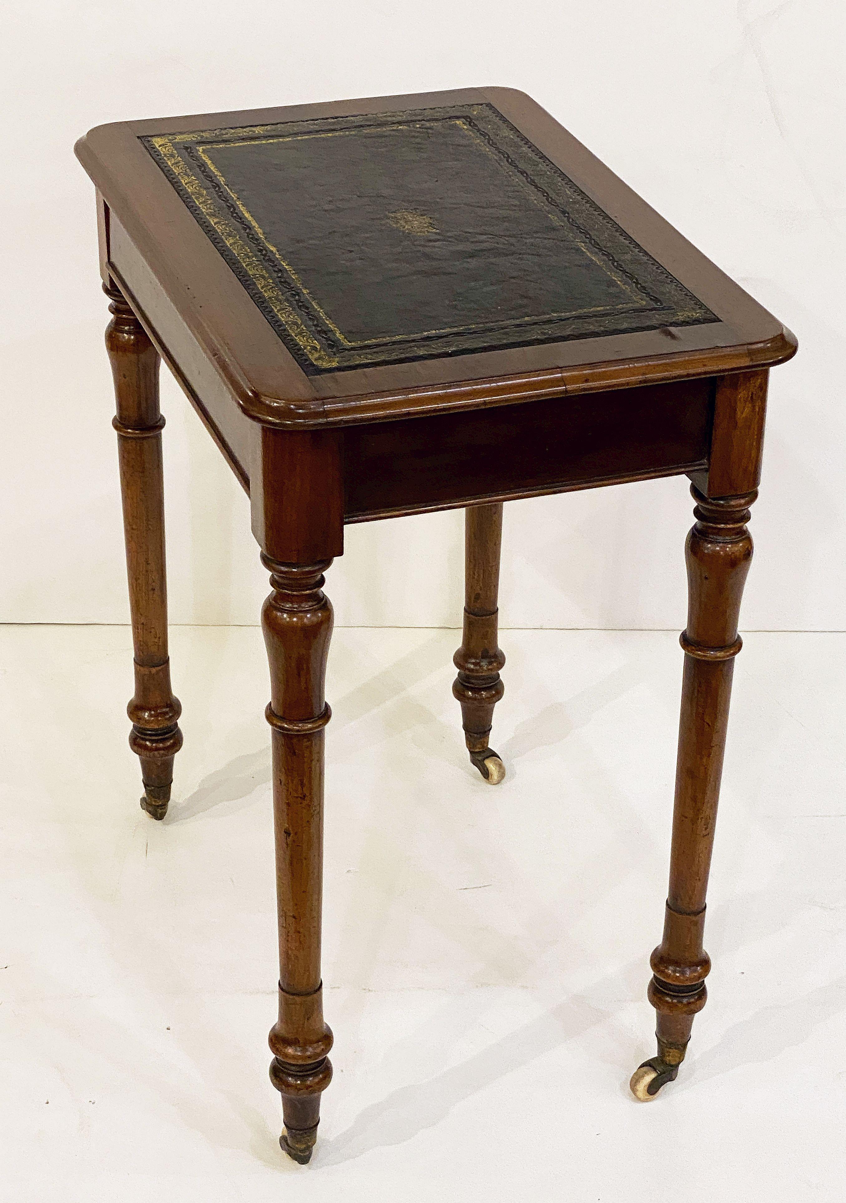 A fine English writing table or desk of mahogany, featuring a rectangular moulded mahogany and gilt embossed black leather inset top over a frieze of one drawer, and set upon four turned legs with original rolling casters.