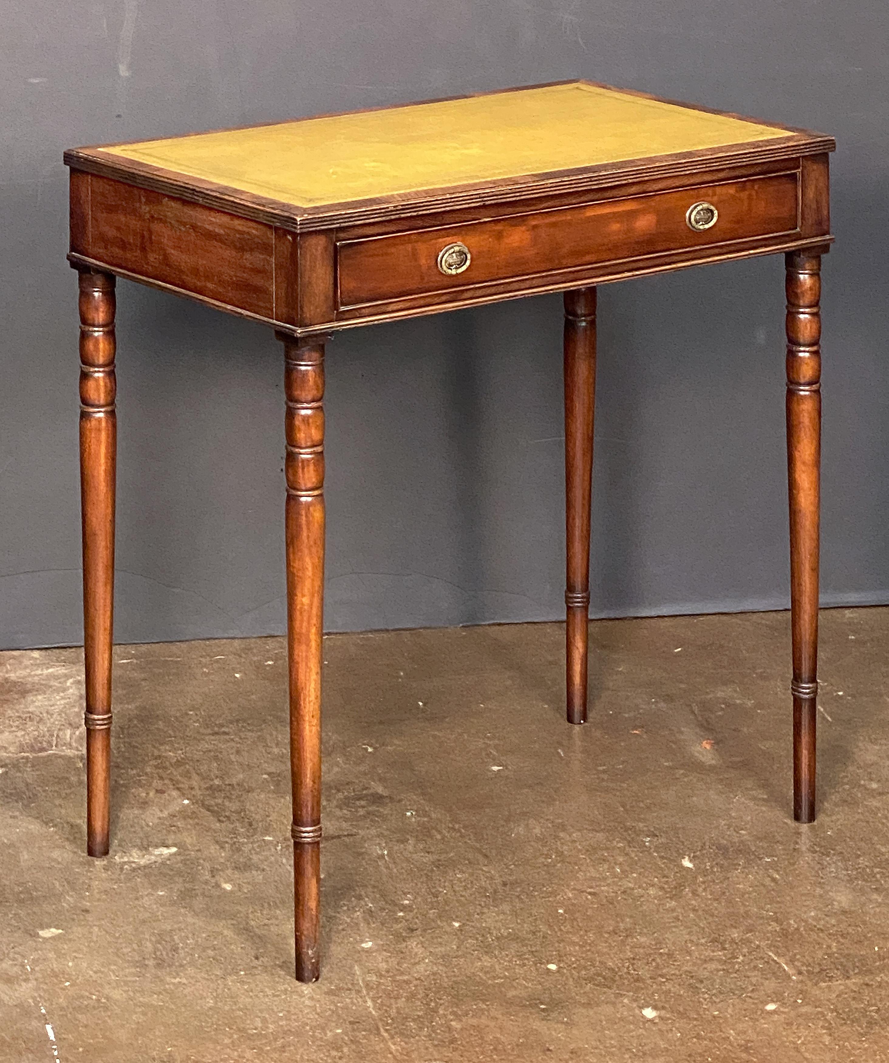 A fine small English writing table or desk of mahogany from the late 19th century, featuring an inset embossed leather top with flame mahogany surround and reeded edge, over a frieze of one beaded long drawer, with brass hardware, and standing on
