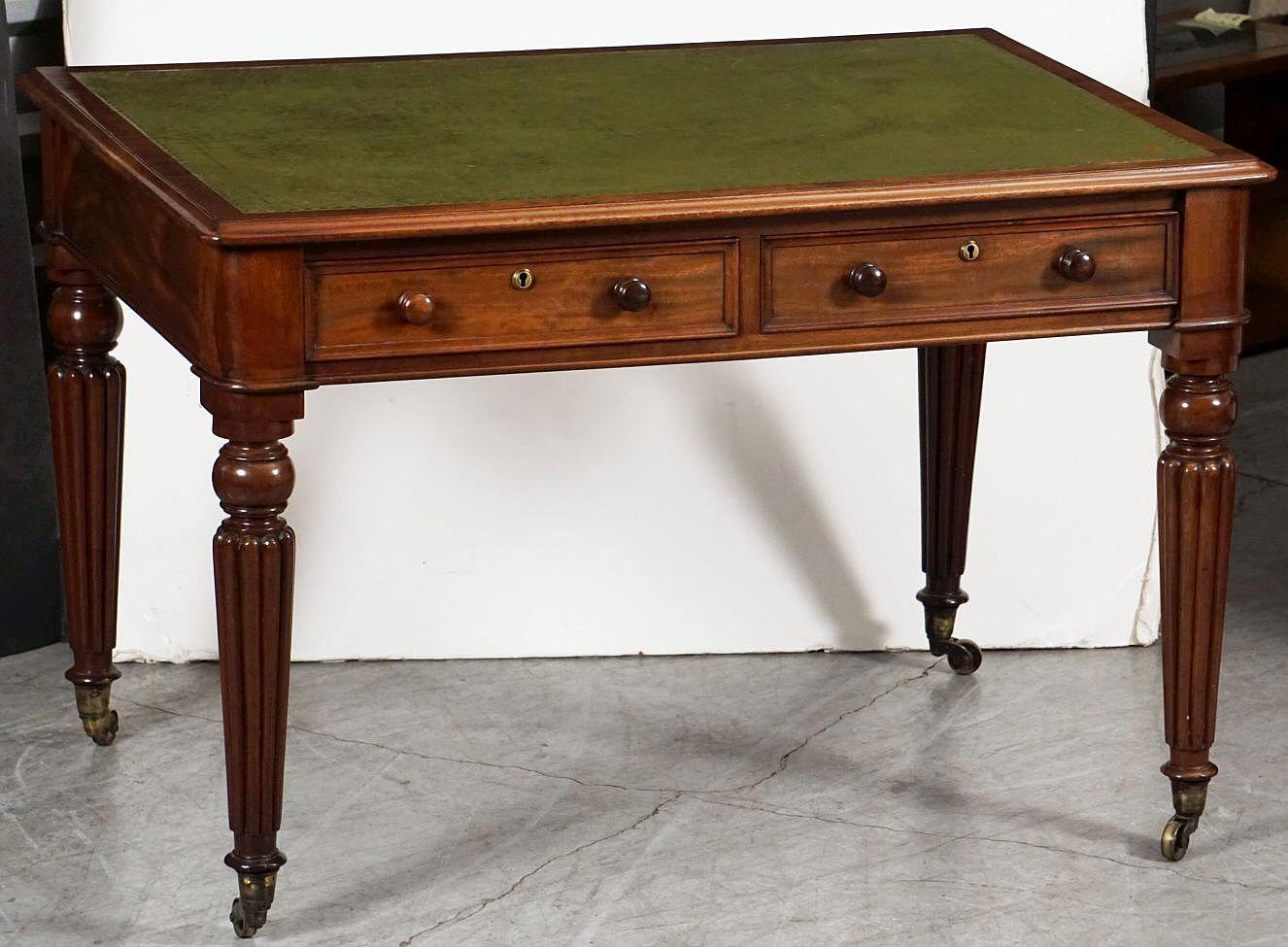 A fine English writing table or desk of patinated mahogany from the William IV period - featuring a moulded rectangular top with a handsome embossed leather writing surface, over a frieze of two fitted and framed drawers - each with round