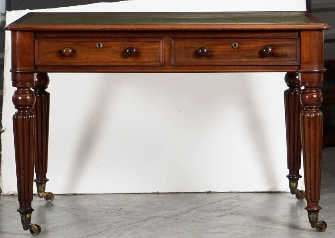 A fine English writing table or desk of patinated mahogany in the William IV style - featuring a moulded rectangular top with a handsome embossed leather writing surface, over a frieze of two fitted and framed drawers - each with round escutcheons
