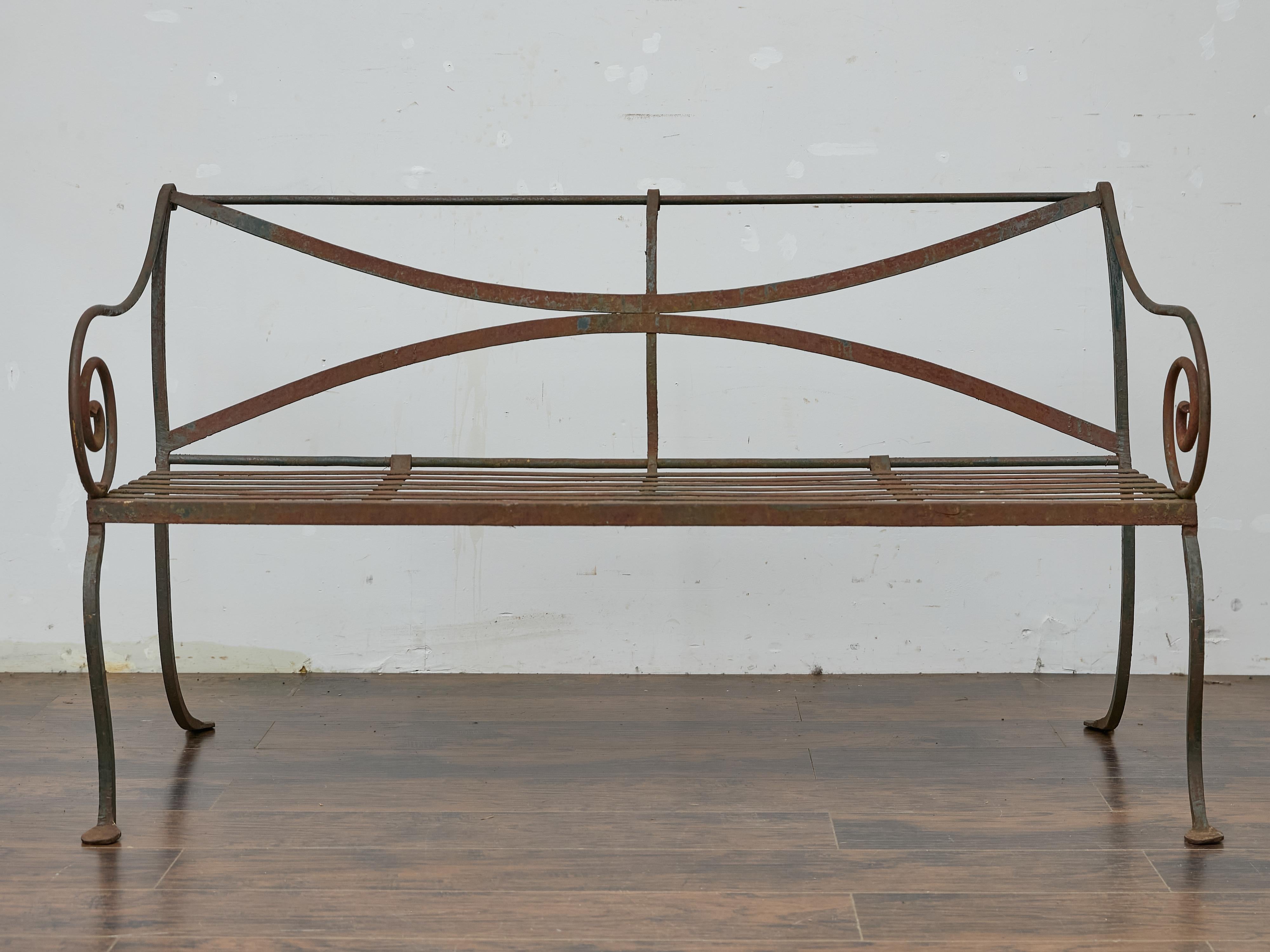 Evoking the charm of an English garden, this wrought iron bench from circa 1920 features graceful lines and a timeworn patina that speaks to its age and authenticity. The backrest is framed with intersecting curved bars that create an elegant