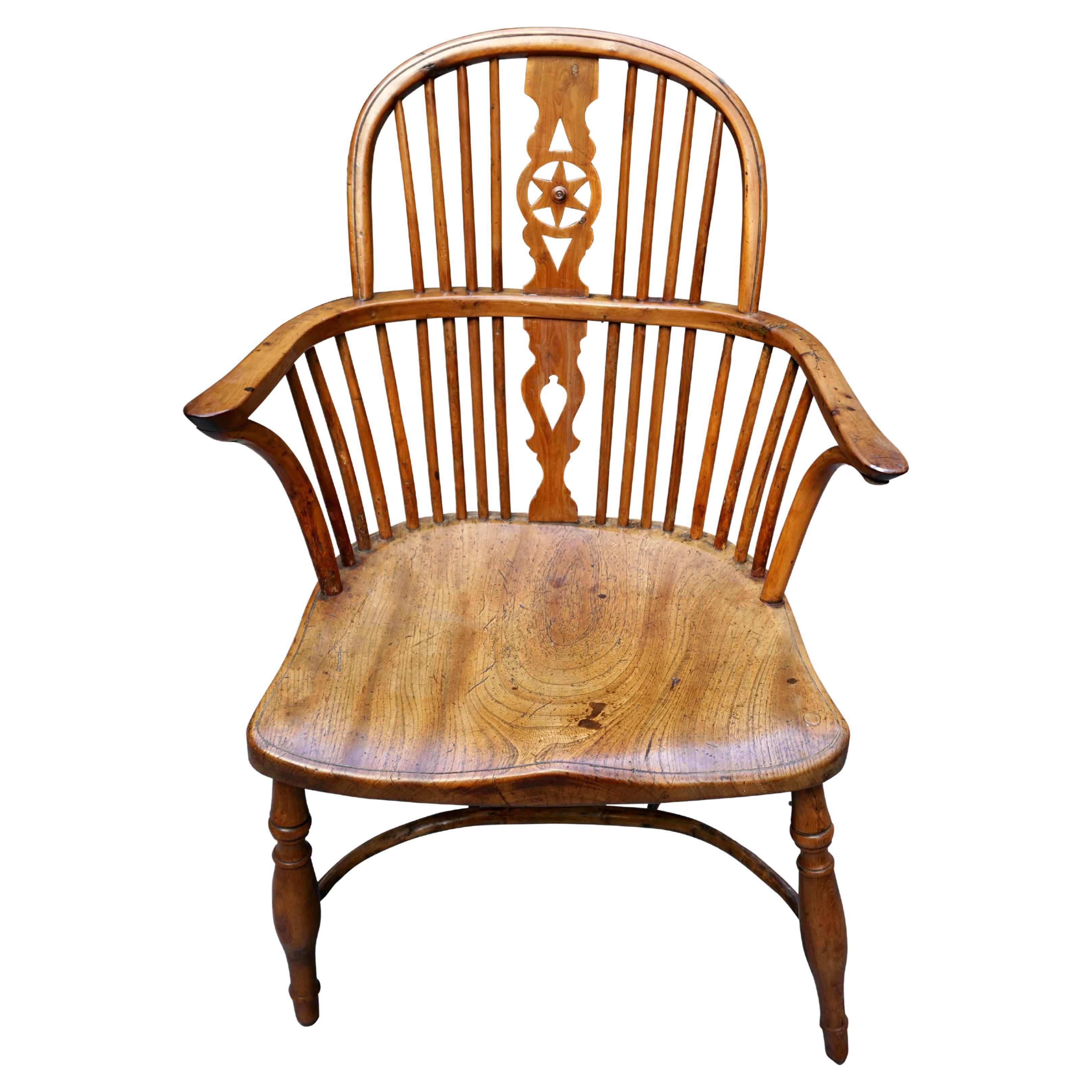 A charming English provincial yew wood and hickory windsor arm chair with a saddle seat, the splat back centered by a star, the legs joined by a crinoline stretcher. Circa 1840. Old repairs. This piece has great character!.