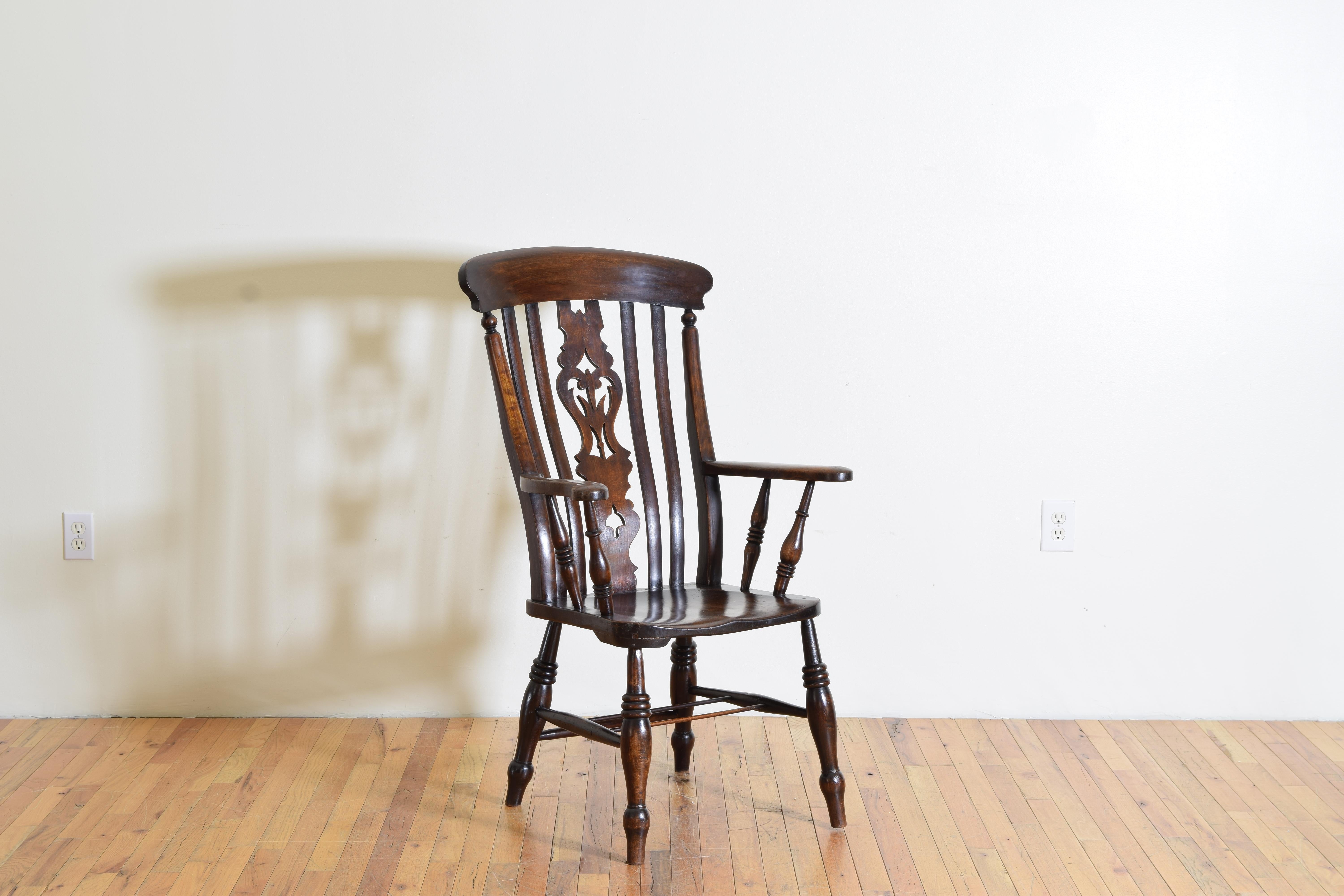 this lovely yew-wood chair from the 1st half of the 19th century has a shaped back with long vertical spindles on either side of a central back splat, with raised arms above a contoured seat, the seat raised on turned legs that are joined by slender