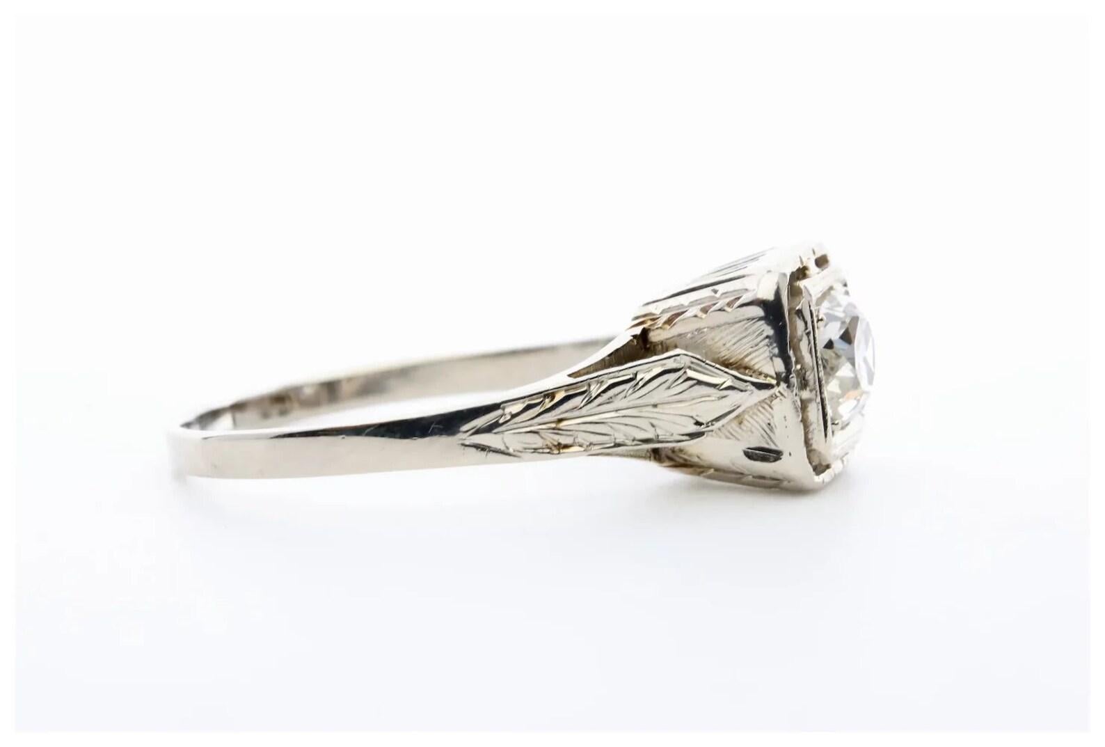 A handmade Art Deco period diamond solitaire engagement ring in 14 karat white gold. Centering this ring is a 0.52 carat old mine cut diamond of H color, SI1 clarity. The mounting features pierced filigree work complemented by hand engraved