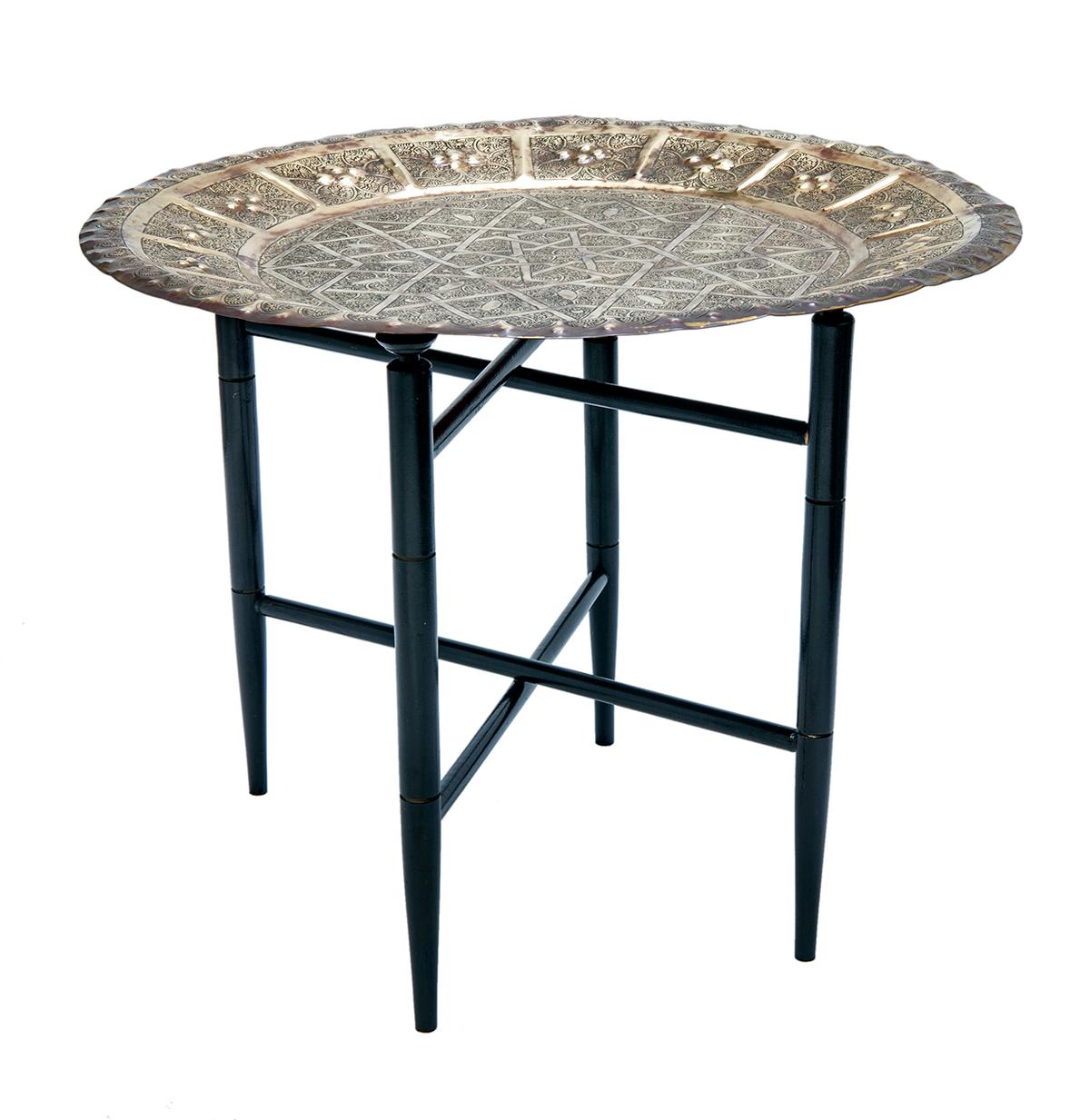 Engraved brass tray table with hand tooled brass tray top in an intricate geometric pattern. The ebony base is accented with gold. and folding teak base. Folds flat when needed.
 