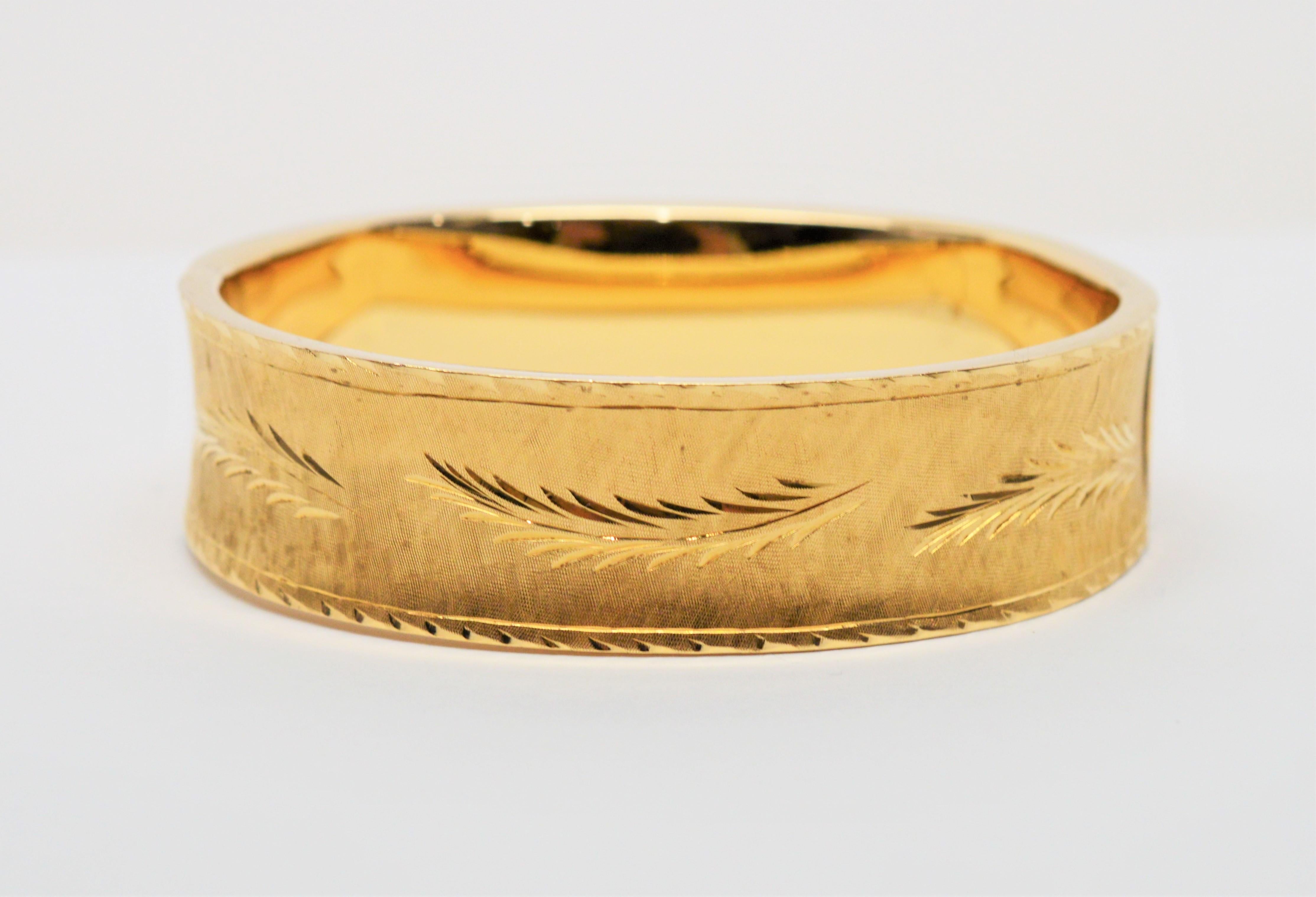 Artistry thru the use of texture and shine are the highlights of this hand engraved fourteen carat 14K yellow gold bangle bracelet.  Measuring  2-1/2 x 2-1/4 inches and approximately 1/2 inch wide, a bright and elegant engraved leaf design encircles
