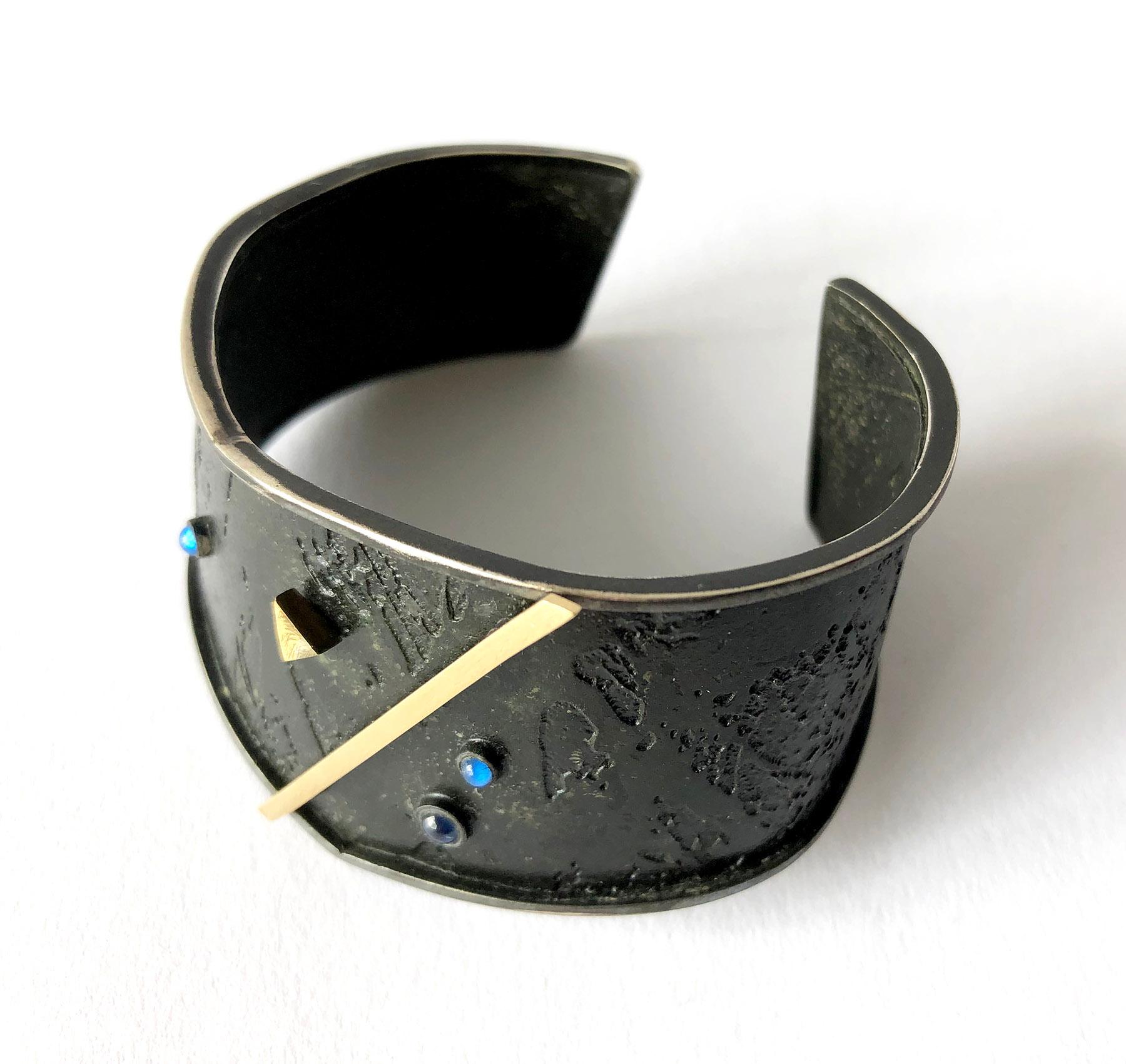 Post modernist cuff bracelet created by Enid Kaplan of New York City, circa 1984.  Bracelet is comprised of oxidized textured silver with floating blue sapphire cabochons and 18k gold geometric accents.  Inner length of the bracelet is 5.25