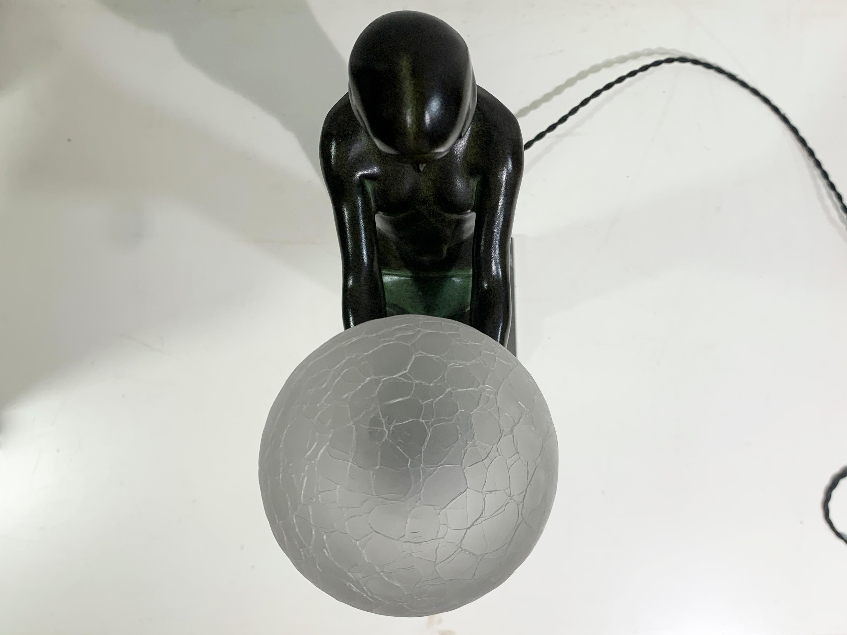 Enigme is an Art Deco style figural table lamp featuring a seated nude holding a glass shade, signed by M. Le Verrier and marked with the foundry's imprint 