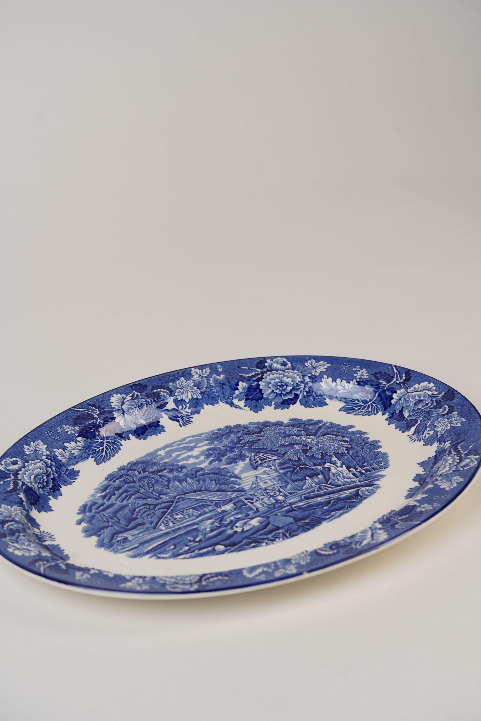 Ce plat ovale bleu et blanc d'Enoch Wood est un exemple intemporel de la vaisselle à transfert anglaise dans toute sa splendeur. Ce qui rend cette pièce vraiment spéciale, c'est sa scène pastorale complexe, un hommage à la vie rurale anglaise,