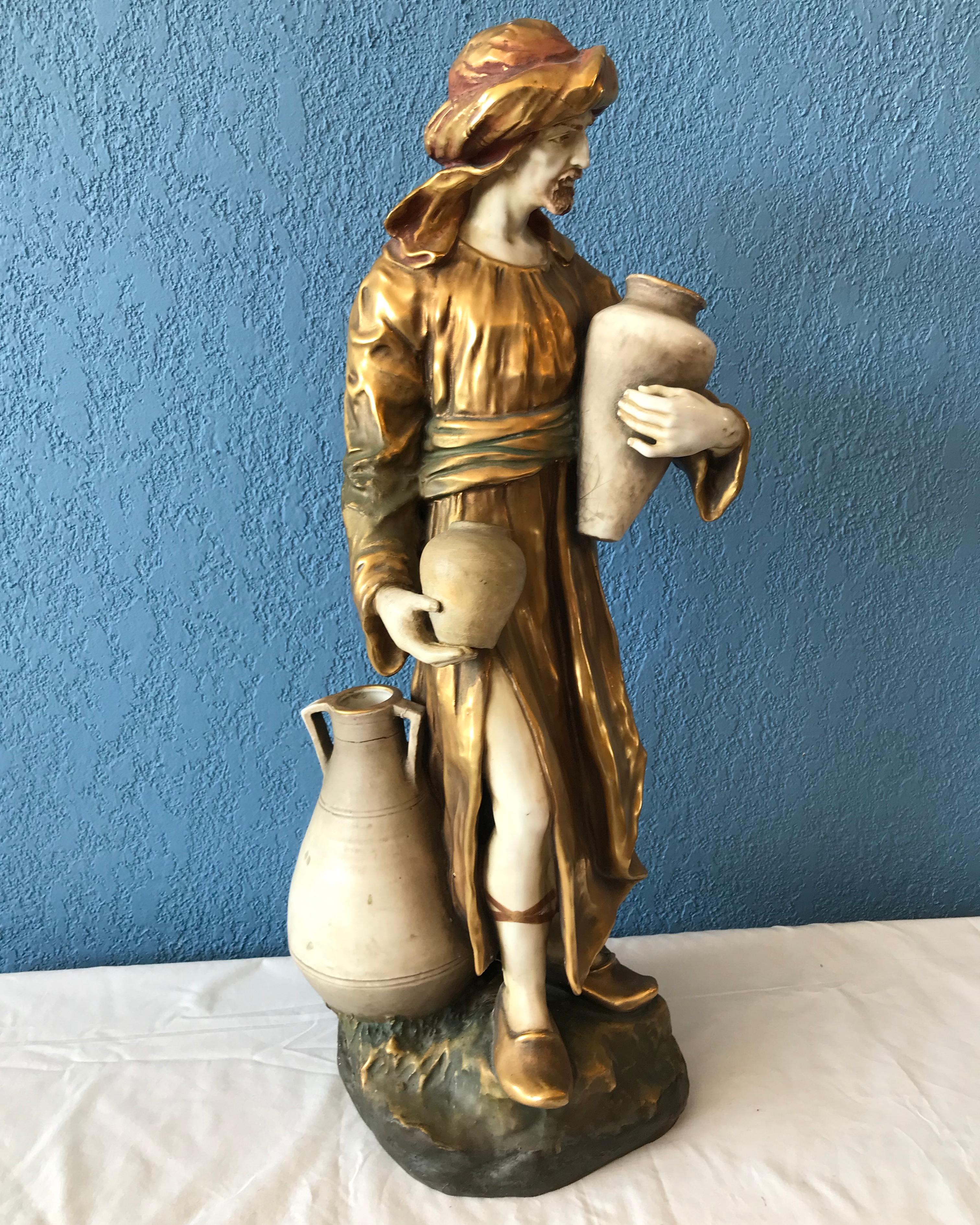 In the style of Amphora and other Bohemian creators. The figure is garbed in gilded robe and turban.
He is posed holding 2 jugs, a third at his feet. 
A bold and dramatic piece.