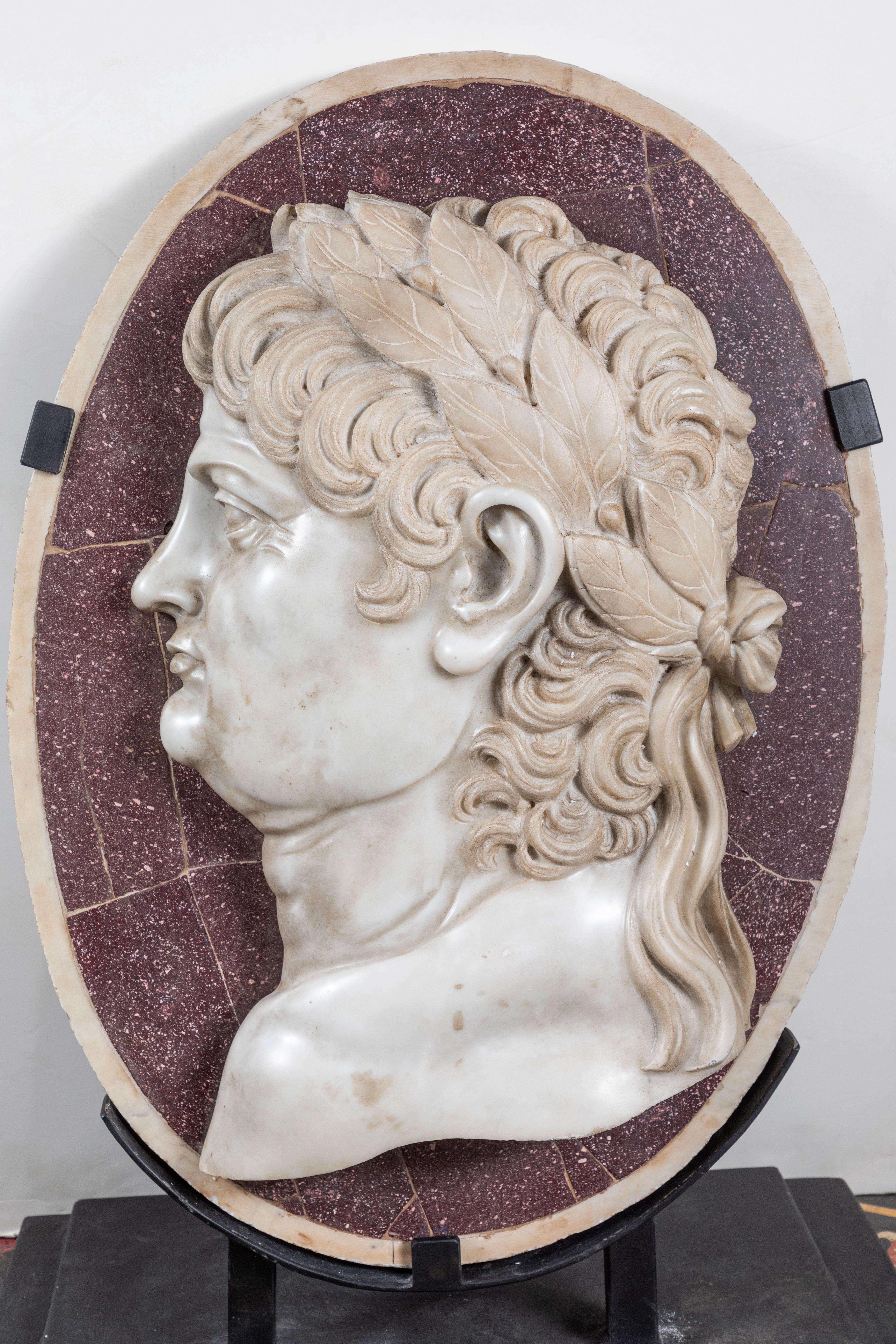 Grand scale and regal, circa 1860, hand carved Carrara marble relief medallion featuring the profile of a senator with flowing hair crowned in laurels. He is surrounded by a porphyry veneer and mounted on a custom, steel stand. Made in Rome and then